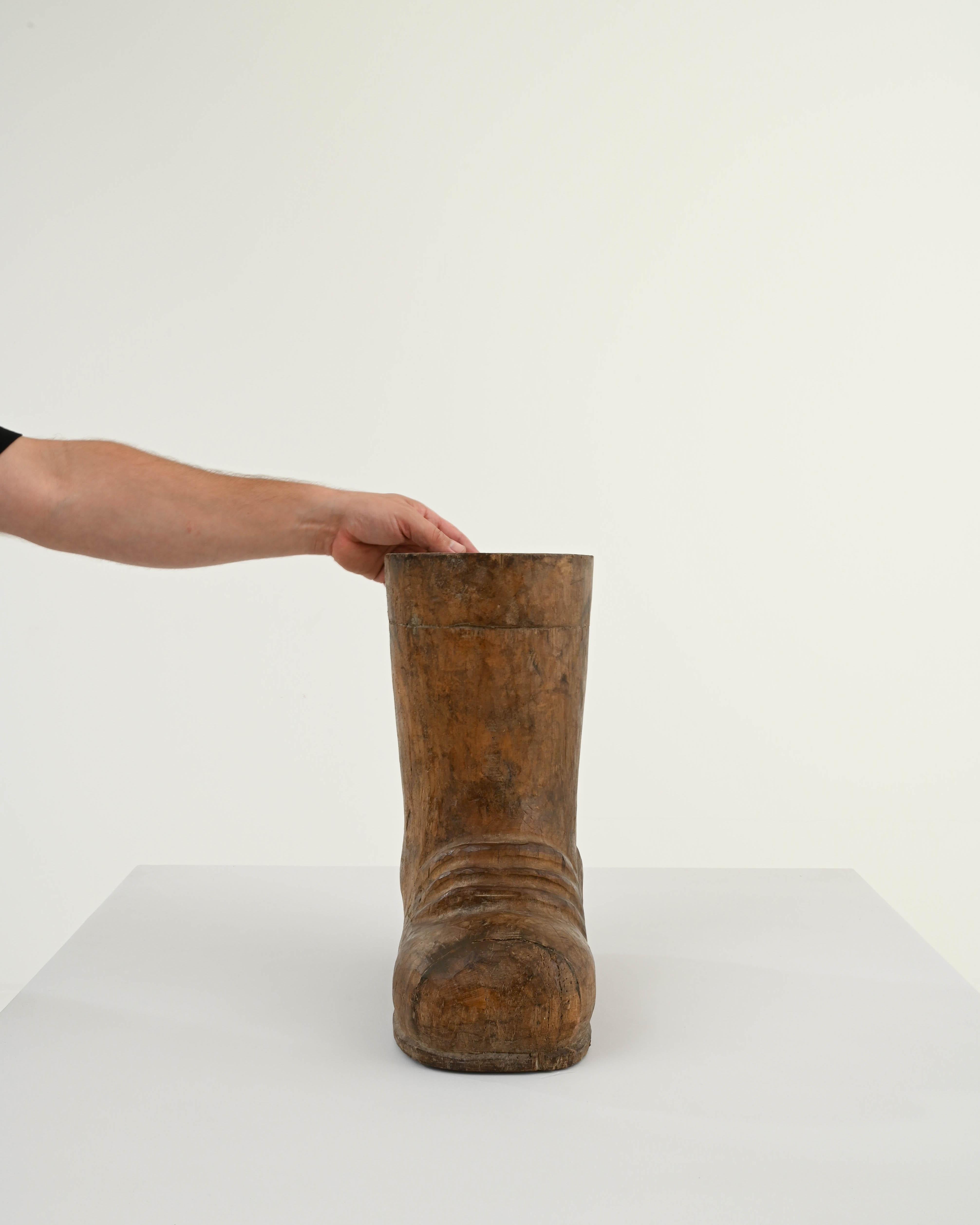 Step into whimsical charm with this 20th Century French Carved Wooden Boot Decoration. Skillfully crafted, this wooden boot captures the essence of a well-worn shoe, complete with intricately carved details that showcase the subtle wrinkles and