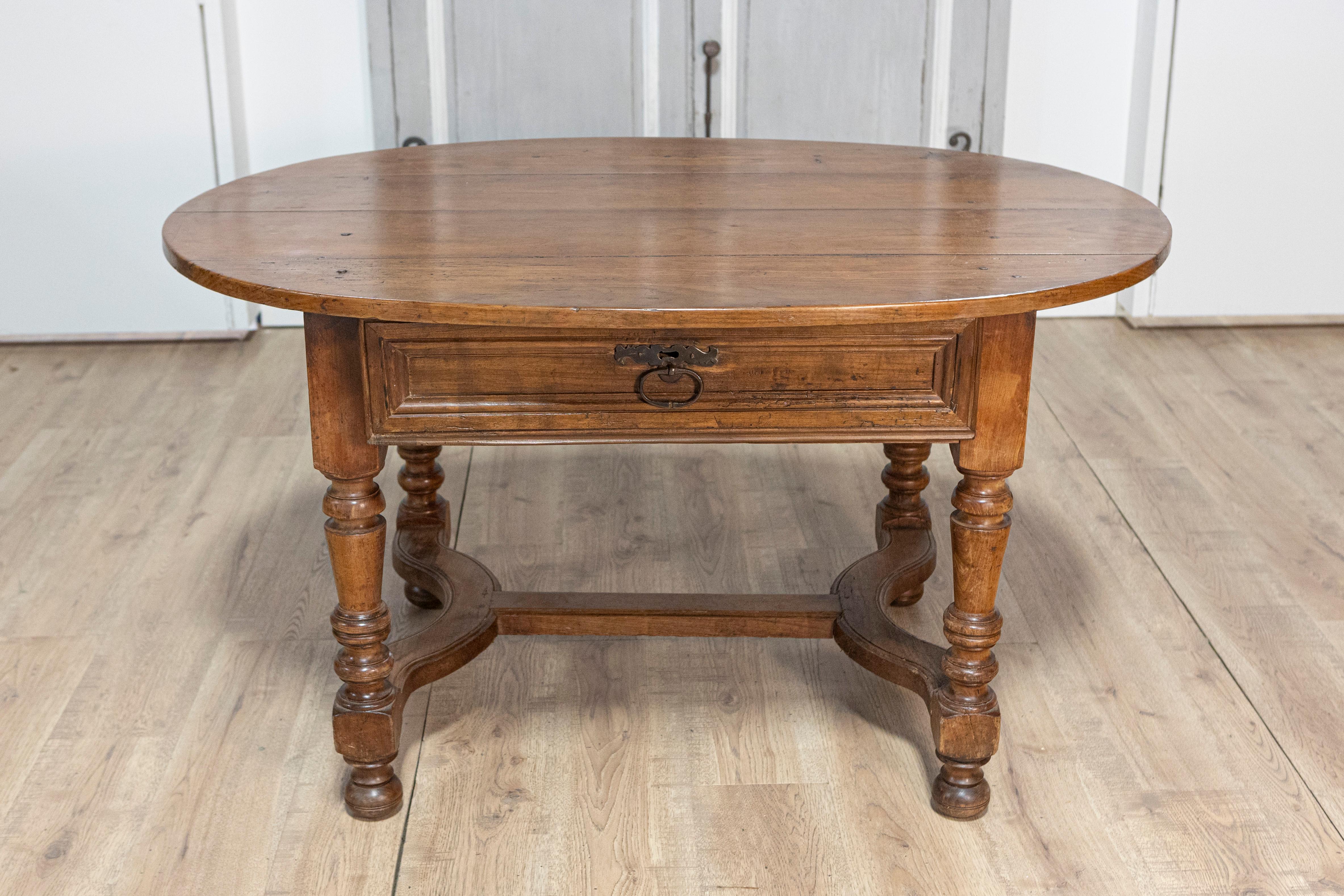 Cette élégante table centrale française du XXe siècle est une pièce magnifiquement fabriquée qui allie fonctionnalité et design français classique. Fabriquée en noyer massif, la table présente un plateau ovale qui met en valeur la beauté naturelle