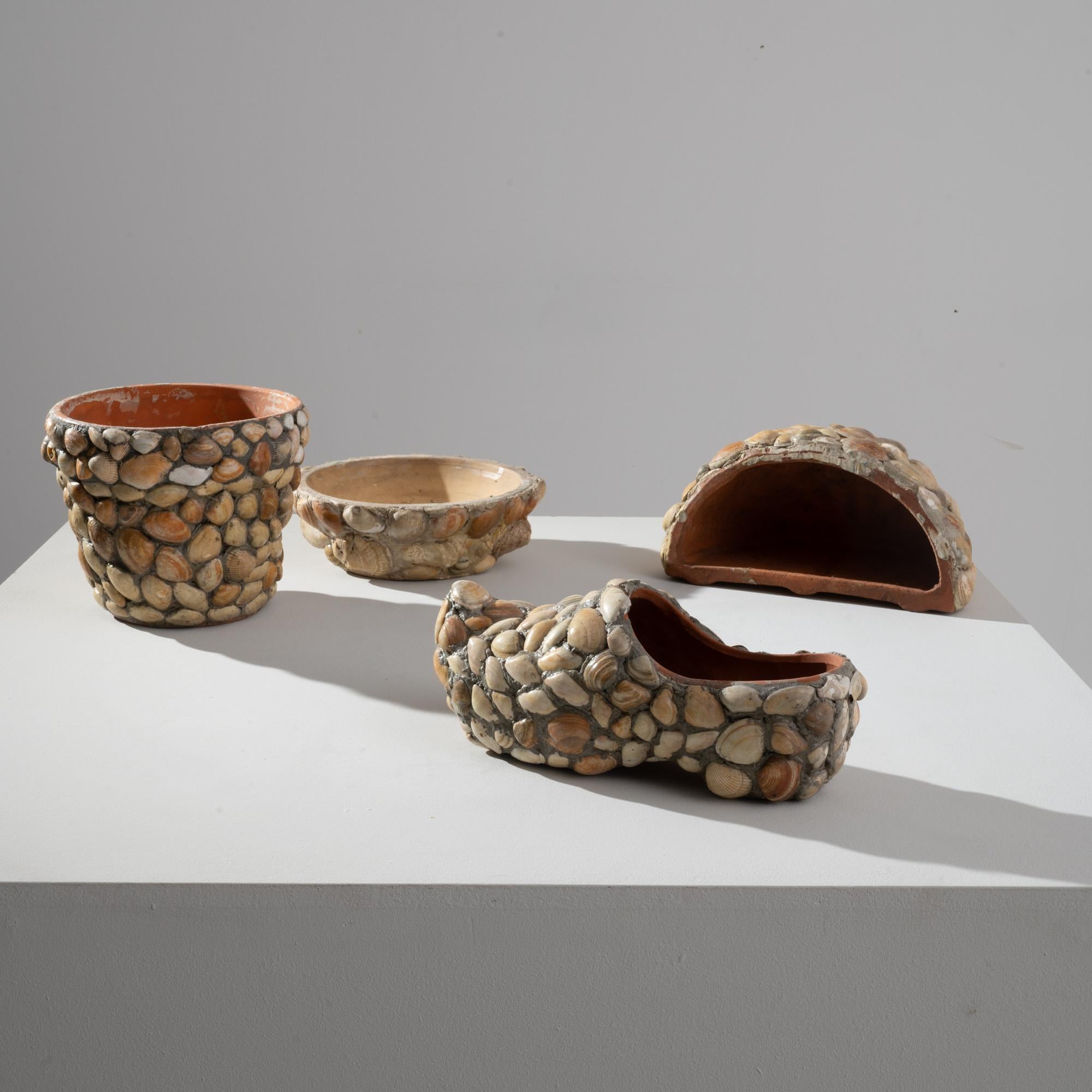 This set of vintage ceramic decorations comprises four pottery objects decorated with local shells: a clog, a bowl, a pot, and a small hemispheric repository. Made in France in the 20th century, these pieces have a handcrafted quality —the shells