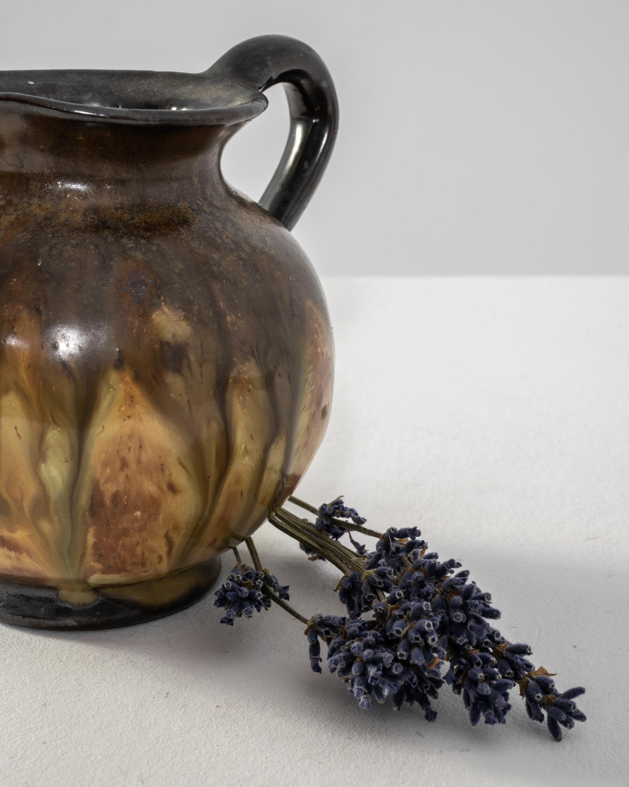 Le charme rustique de cette cruche en céramique française du XXe siècle, ornée d'une glaçure tachetée dans des tons terreux et des touches de moutarde et de bleu pâle. Le bord, le bec et la poignée noirs ajoutent une touche d'élégance à son attrait