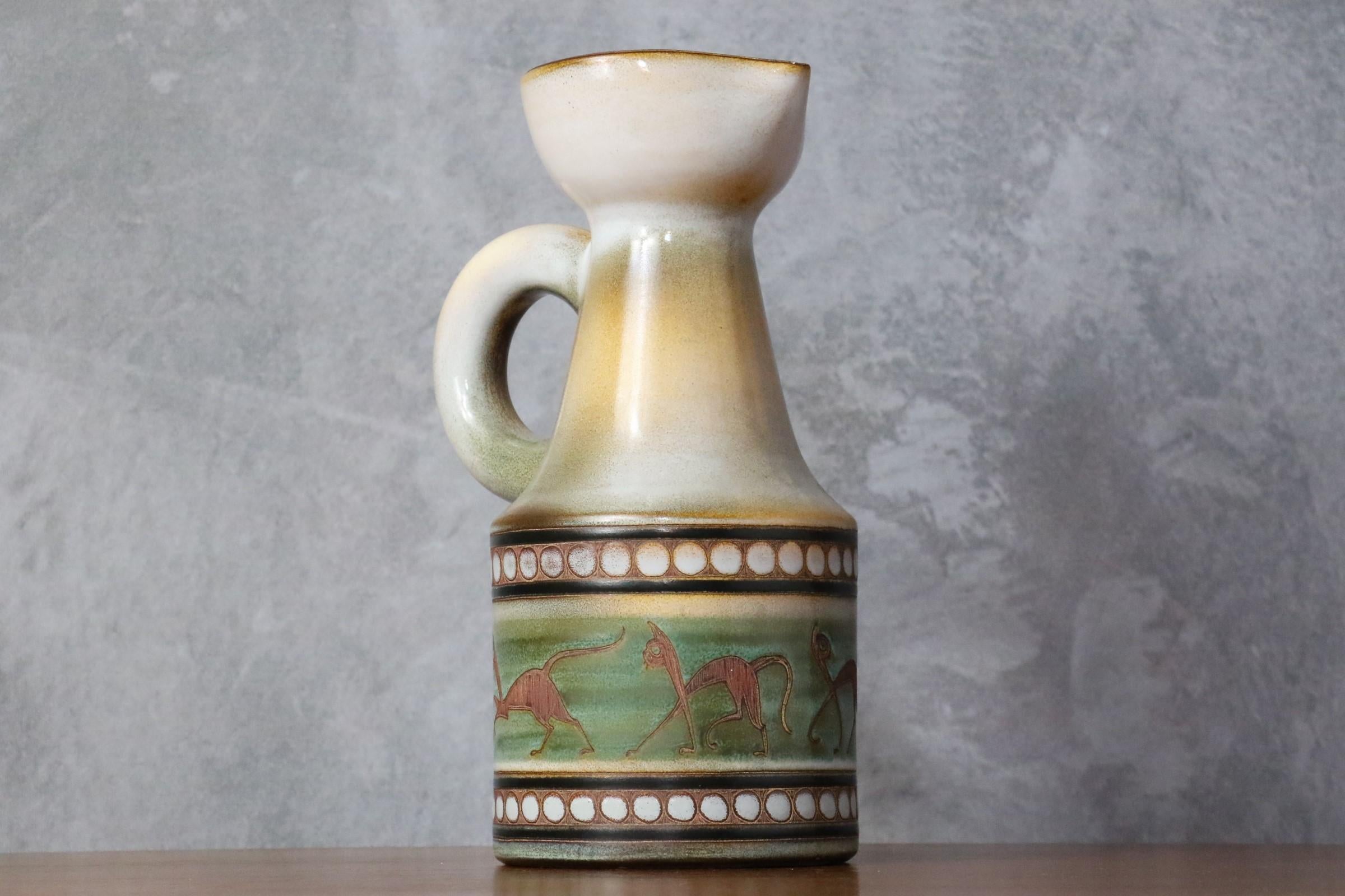 20th century French white ceramic pitcher by René Maurel, 1960's

The pitcher is glazed in a brilliant creamy white. It is decorated with a cats frieze with round motifs and colored in pale tones. 
It is signed under the base. 
It is in a very