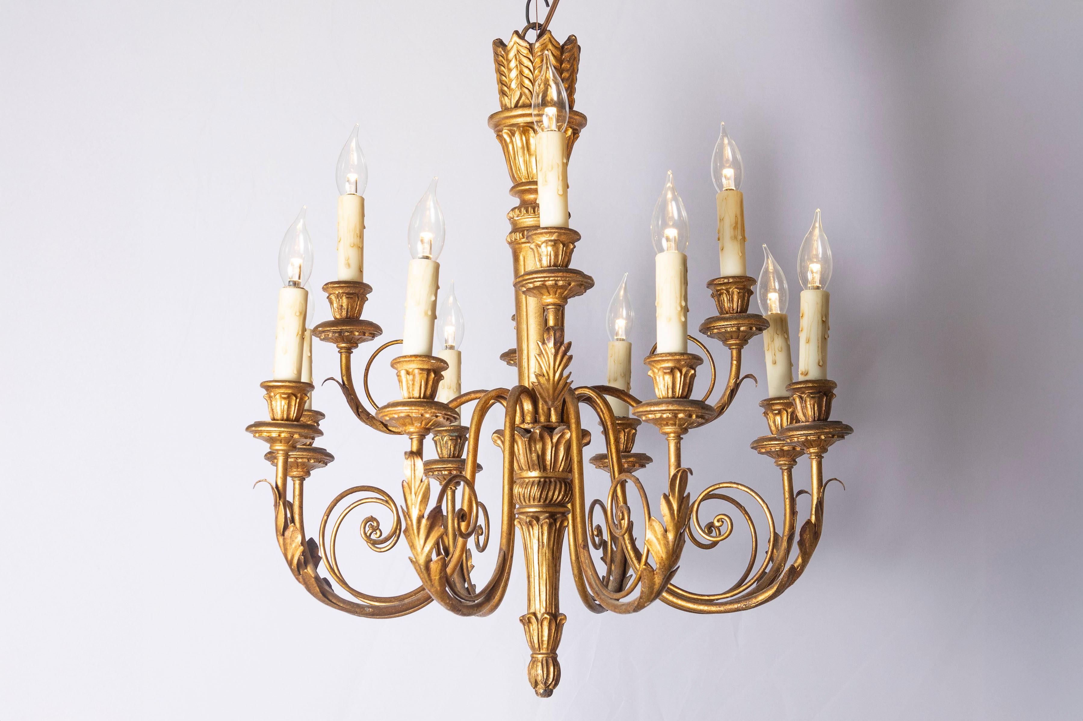 Cet exquis lustre français du XXe siècle incarne la grandeur du style Louis XVI, alliant l'élégance néoclassique à un travail d'orfèvre. Fabriquée en bois et en métal doré, sa colonne centrale présente des motifs cannelés et des feuilles d'acanthe