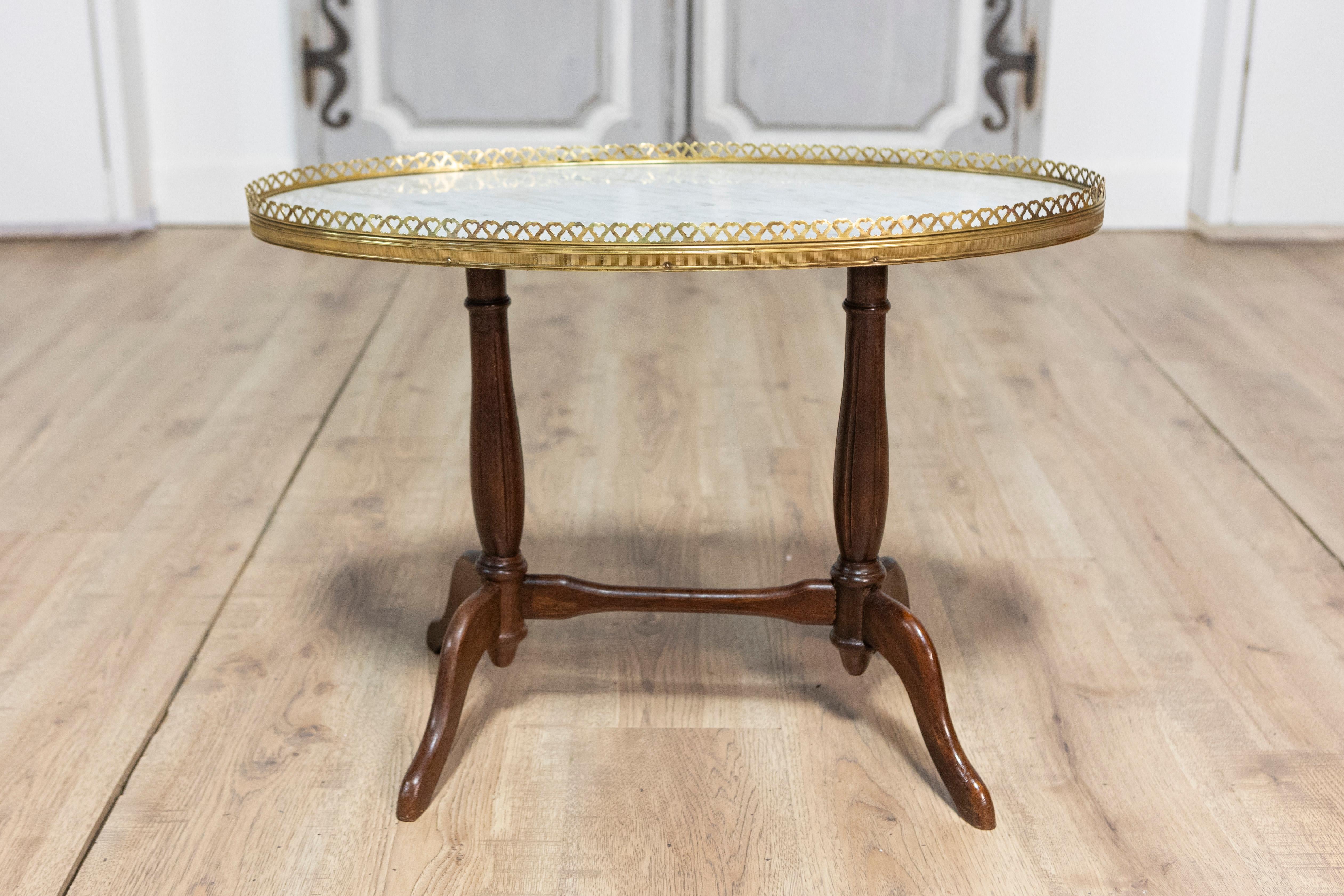 Cette exquise table basse française du début du XXe siècle allie un design simple et élégant à des matériaux intemporels. Le plateau de table de forme ovale est fabriqué en marbre blanc immaculé, encadré par une galerie en laiton complexe aux