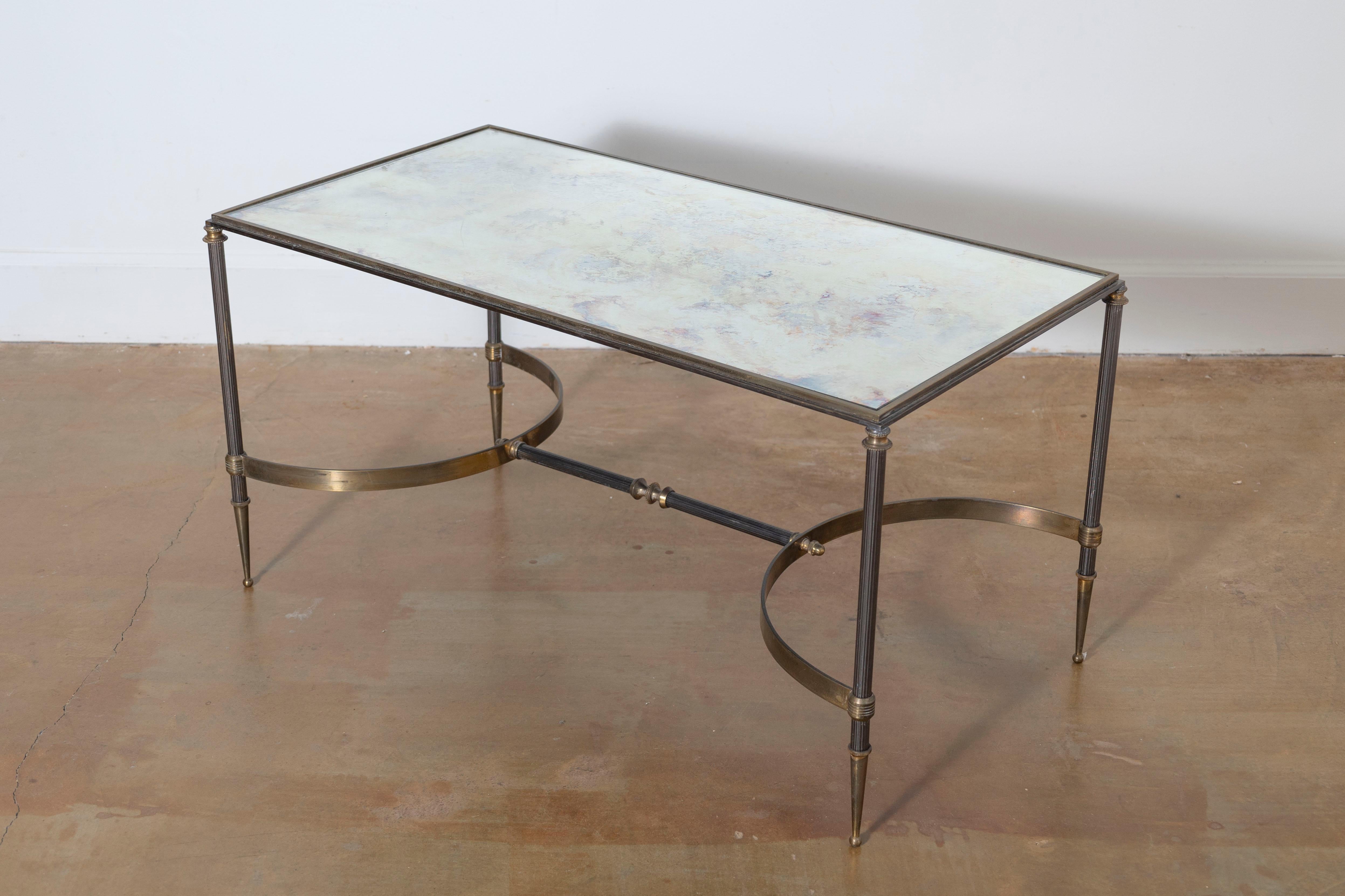 Questo tavolino francese del XX secolo emana una raffinatezza e un'eleganza senza tempo. Il piano rettangolare presenta un pannello di vetro con una parte inferiore testurizzata o dipinta, che aggiunge profondità e un sottile interesse artistico al