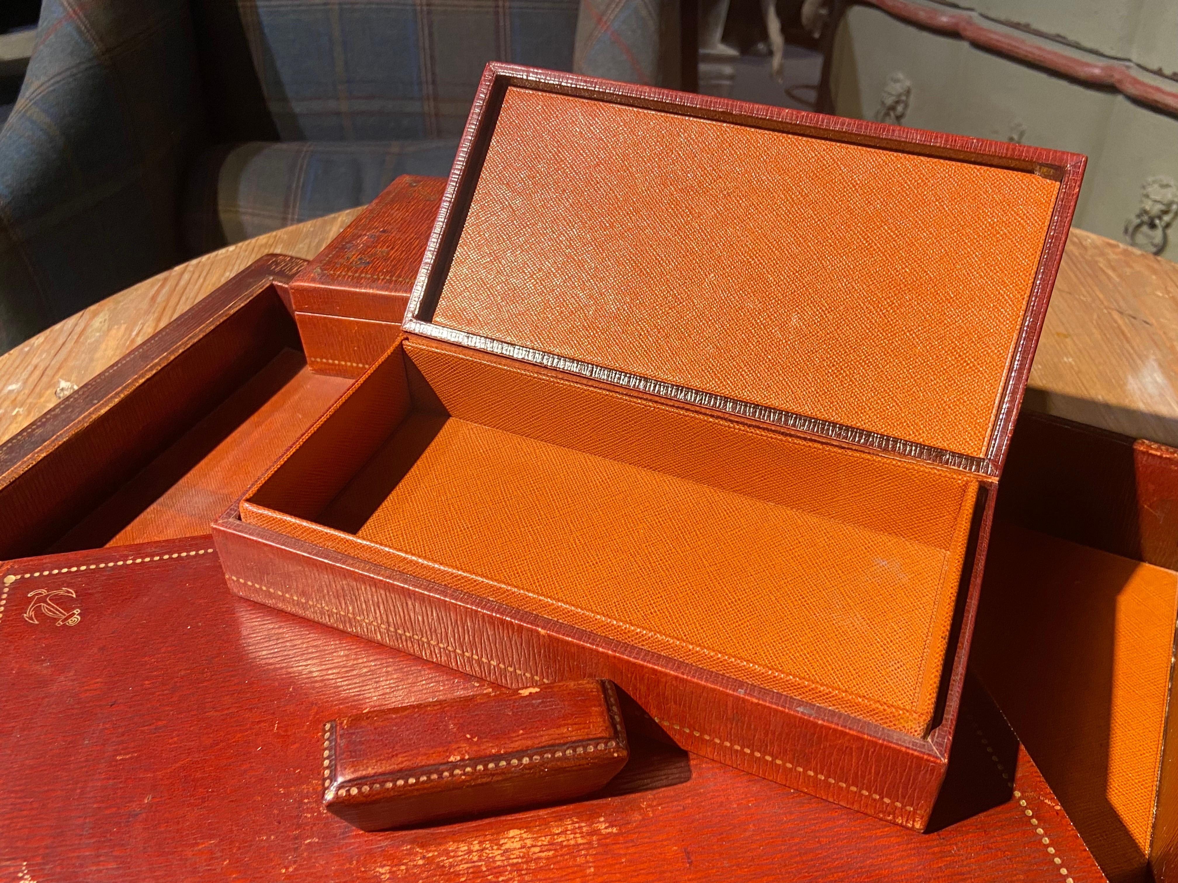 French leather desk set of five pieces all wrapped in genuine leather in special cognac colour. The set contains a large desk pad, a small open paper tray, a bigger paper box with orange leather interior and a cover and two small leather boxes with