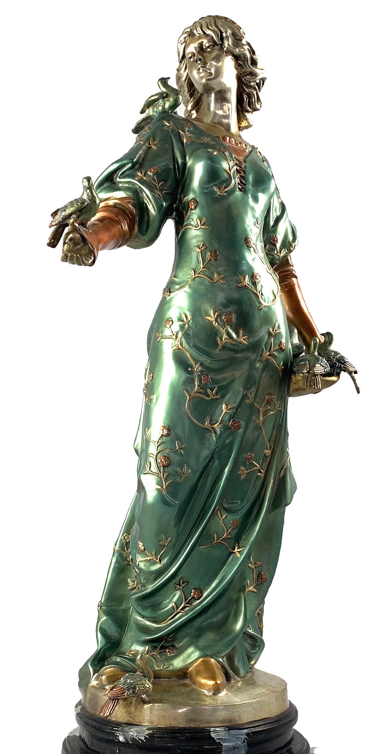 A fine example of cold painted bronze figure of a woman. French 20th century. Cast with flowing robes a small bird perched on her outstretched arm. Decorated in green an gold and supported on a dark green Antico marble base.