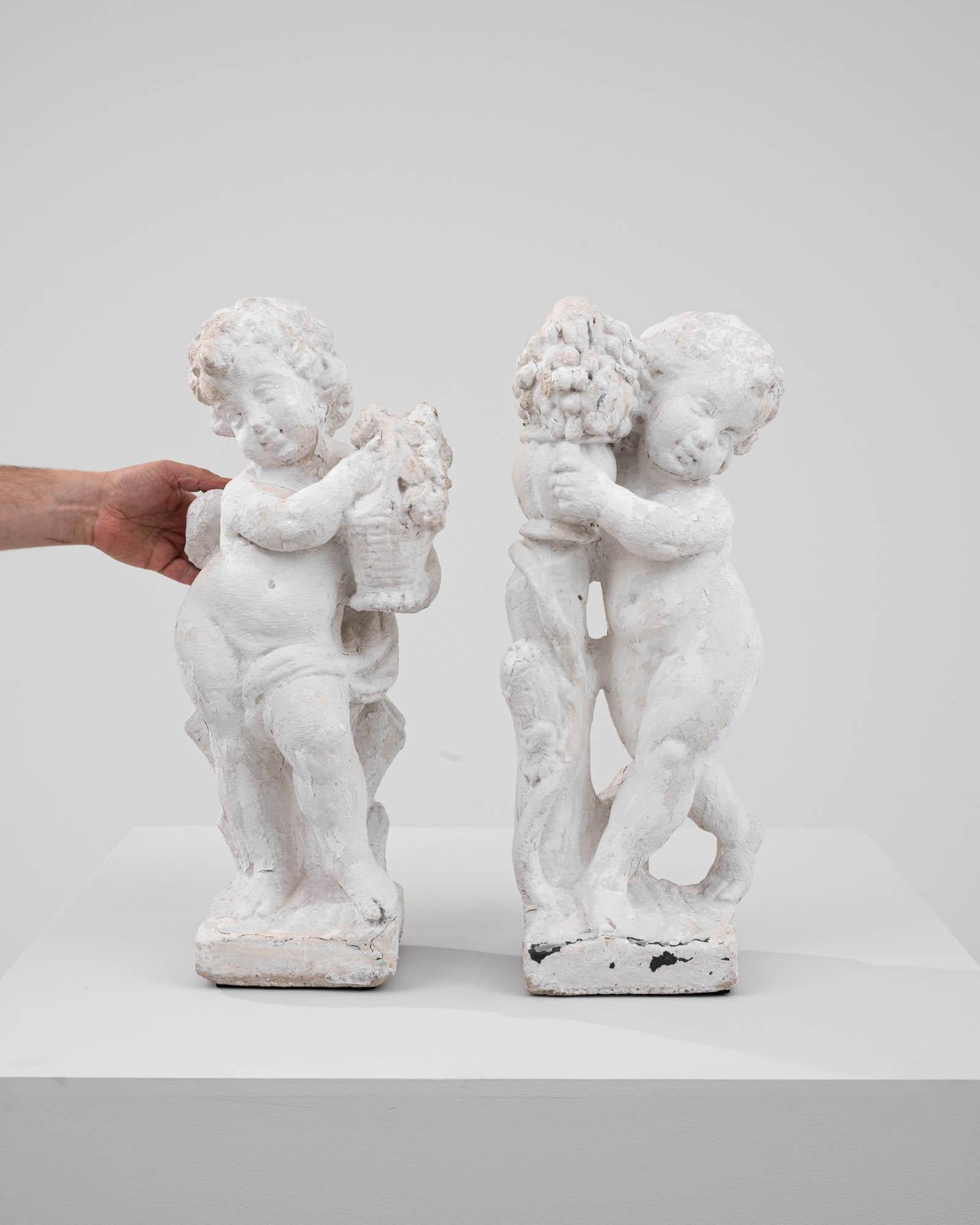 This pair of 20th Century French Concrete Angels captures the essence of pastoral charm, each tenderly clutching a bundle of flowers. The sculptures convey a sense of innocence and playfulness, with the angels' gestures suggesting a moment caught in