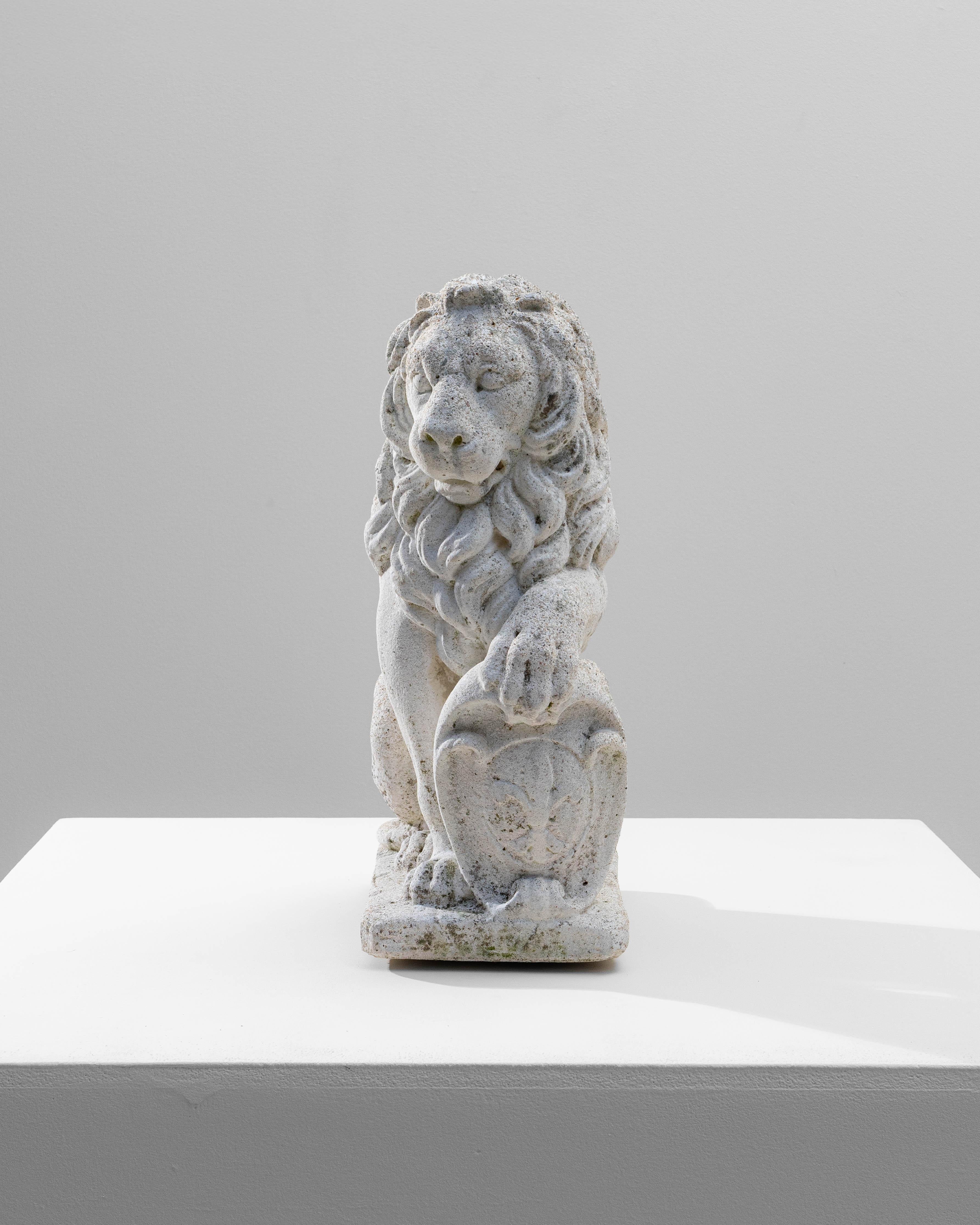 20th Century French Concrete Lion Sculpture. This expressive French lion sculpture, cast in concrete, captures a classic symbol of strength and guardianship with a beautifully weathered presence. The lion is depicted seated with one paw resting on