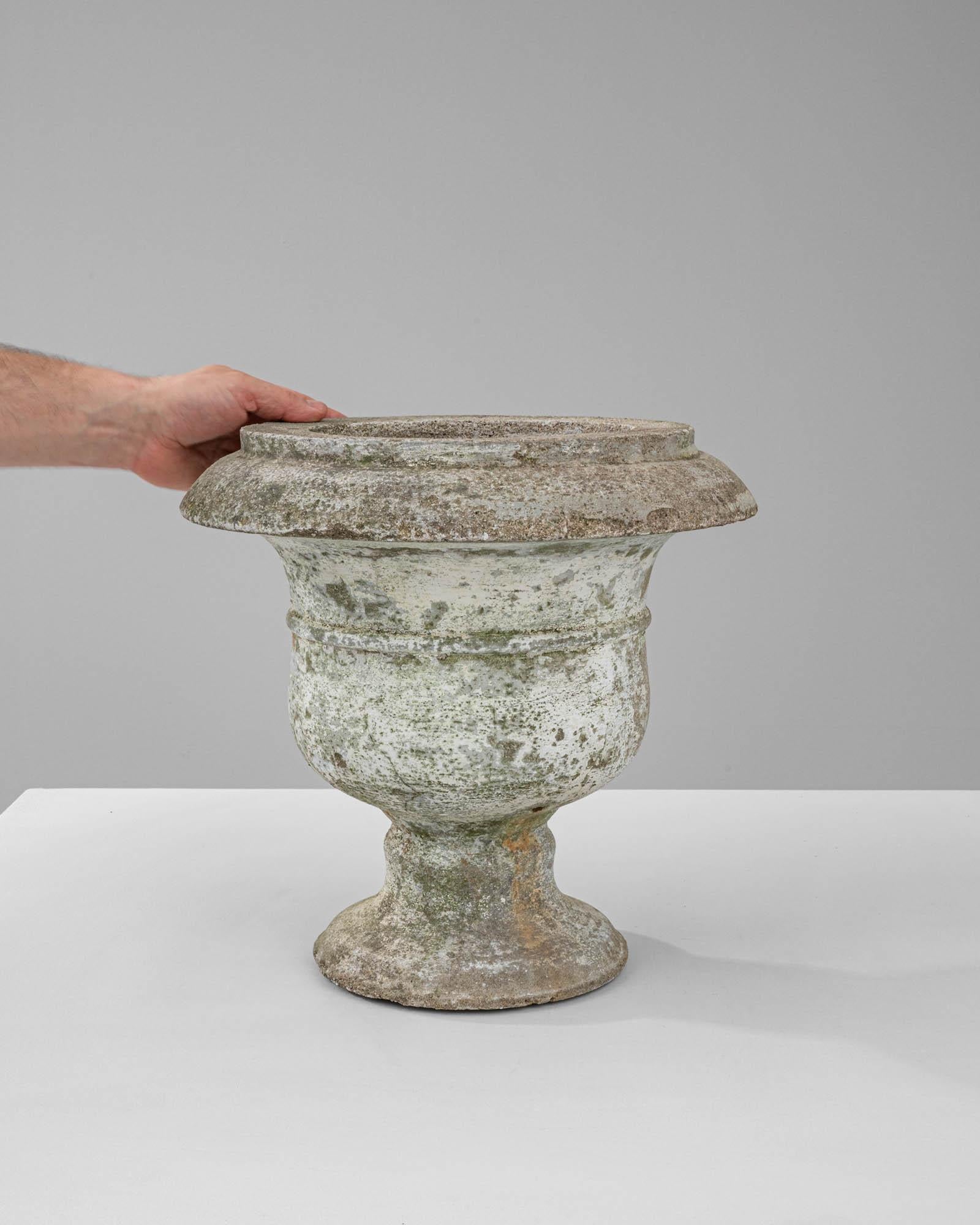 Step into the past with this exquisite 20th-century French concrete planter, a piece rich in history and texture. The planter's grand, classical urn shape, complete with a flared rim and robust pedestal base, offers an air of formality and grandeur