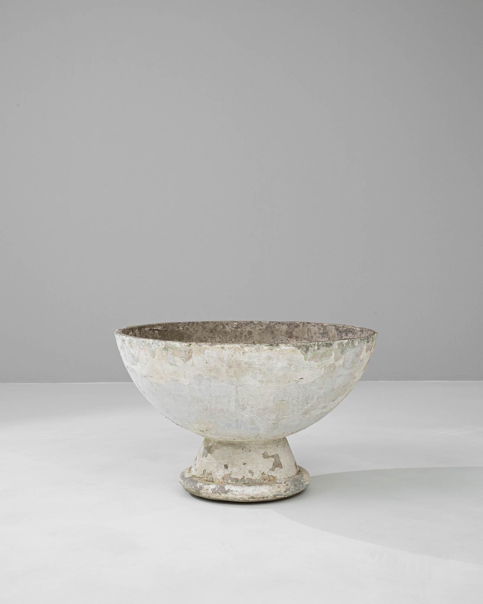 With its elegant bowl shape and sturdy pedestal, this 20th-century French concrete planter is a testament to timeless design. The worn patina, with its peeled layers and natural wear, adds a sense of history and character, suggesting it has been a
