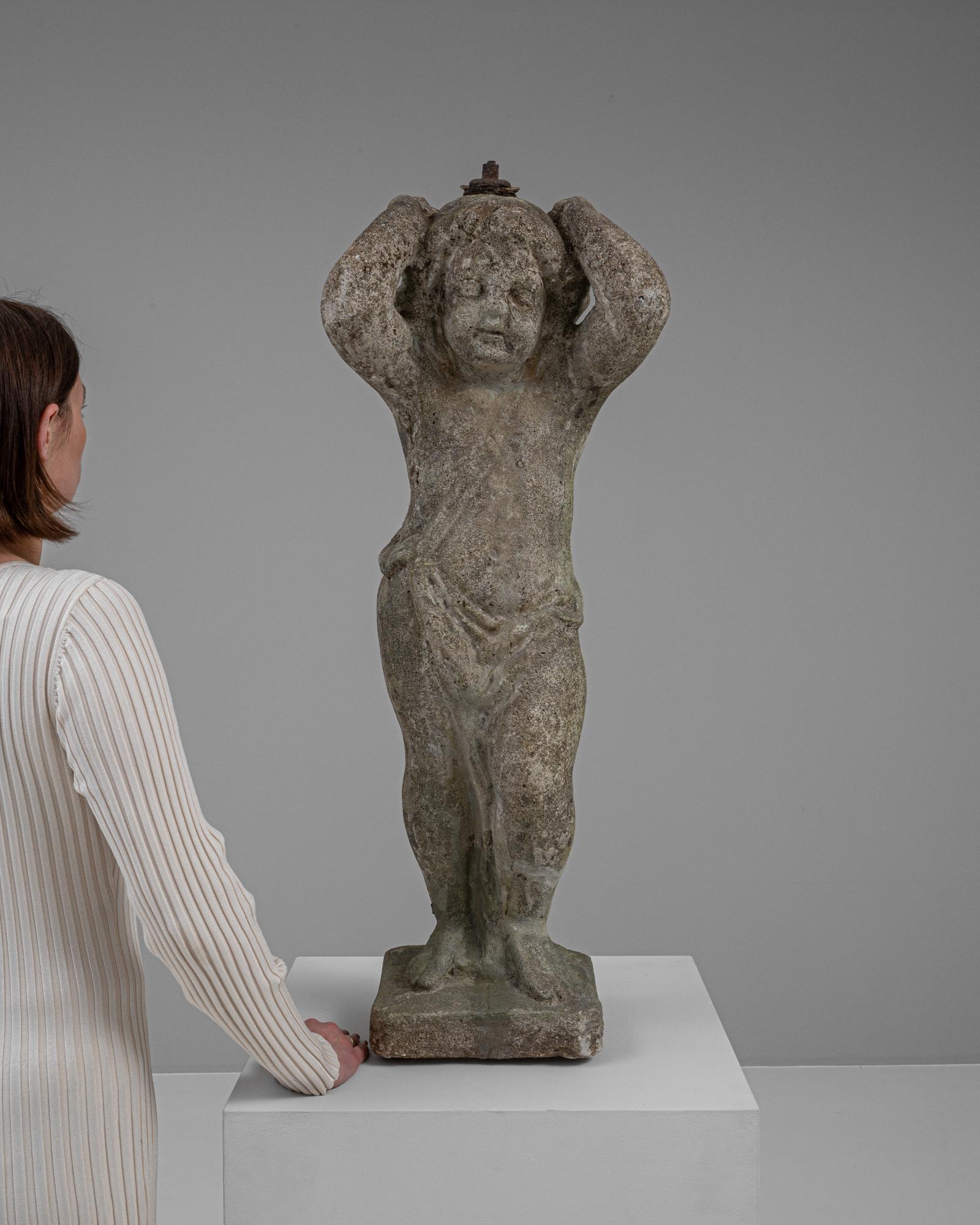 Questa affascinante scultura in cemento del XX secolo presenta un'espressiva rappresentazione di un bambino in una posa di spensierato abbandono. La superficie strutturata e rovinata dal tempo del cemento conferisce un profondo senso di atemporalità