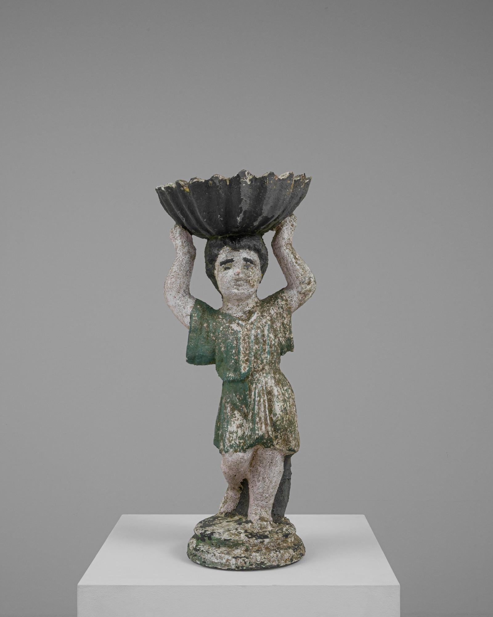 Questa scultura in cemento francese del XX secolo cattura magnificamente lo spirito giocoso di un giovane ragazzo, reso in uno stile rustico e consumato dal tempo. La figura, raffigurata in una posa dinamica con le braccia sollevate per sostenere