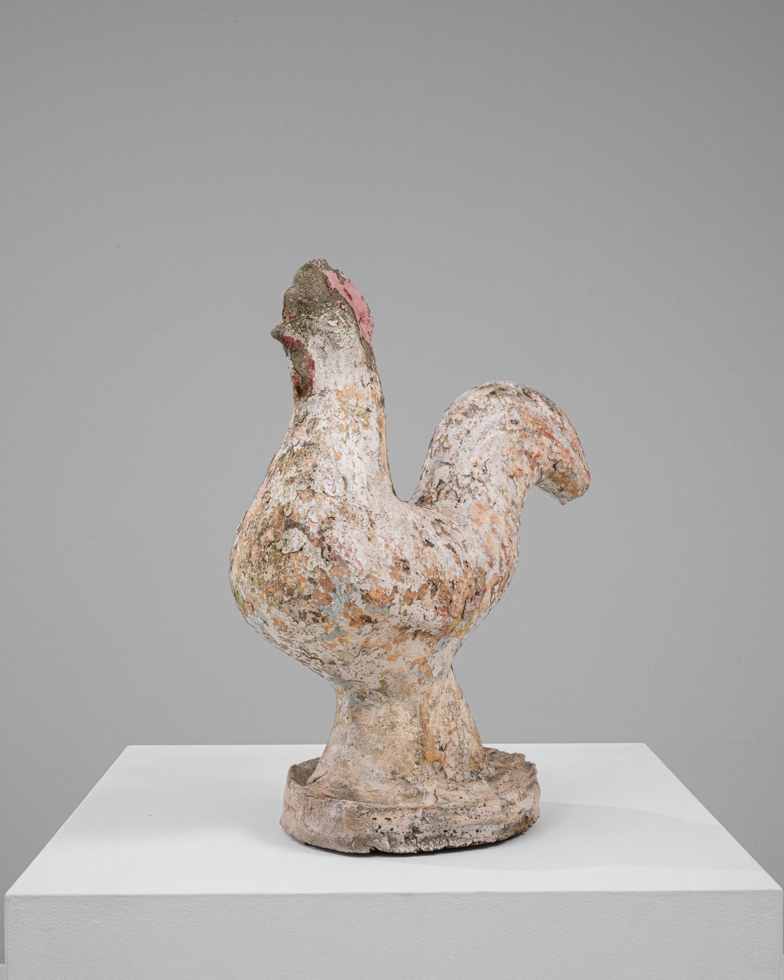 Cette sculpture française en béton du XXe siècle présente un coq au design rustique et usé par les intempéries qui respire le charme et le caractère. La surface texturée de la pièce présente des couches de patine et des teintes moussues, reflétant