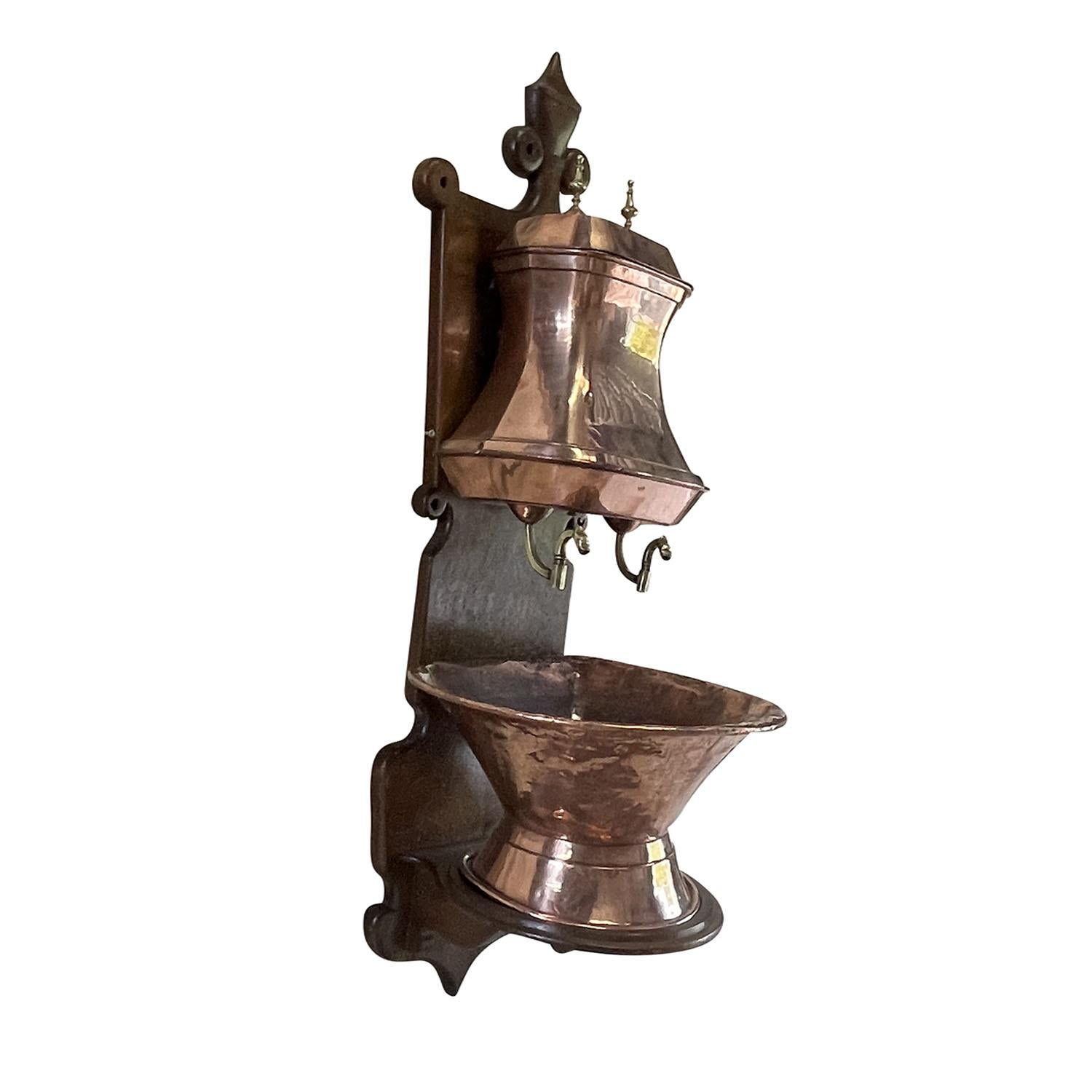 Un antico lavabo o fontana da parete in rame lavorato a mano dell'inizio del XX secolo, in buone condizioni. L'acqua è montata a parete sulla tavola di legno originale. Il lavabo presenta la vasca inferiore originale e il serbatoio superiore con