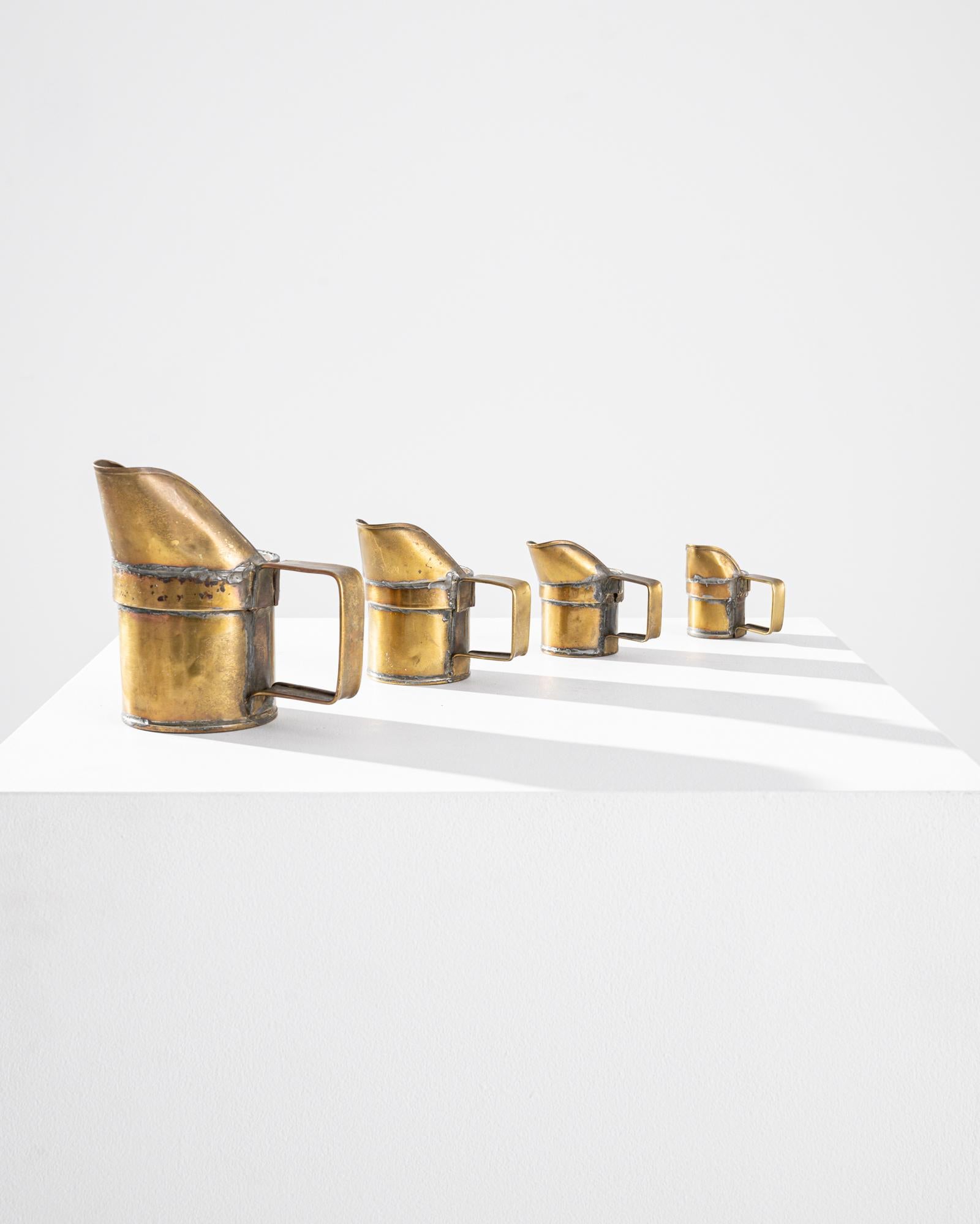 A set of four 20th century copper measurers crafted in France, these antique decorative cups feature an elegant asymmetric folded spout and a striking rectangular handle. Slightly oxidized, the lush finish of the copper exhibits a deep gilded tone