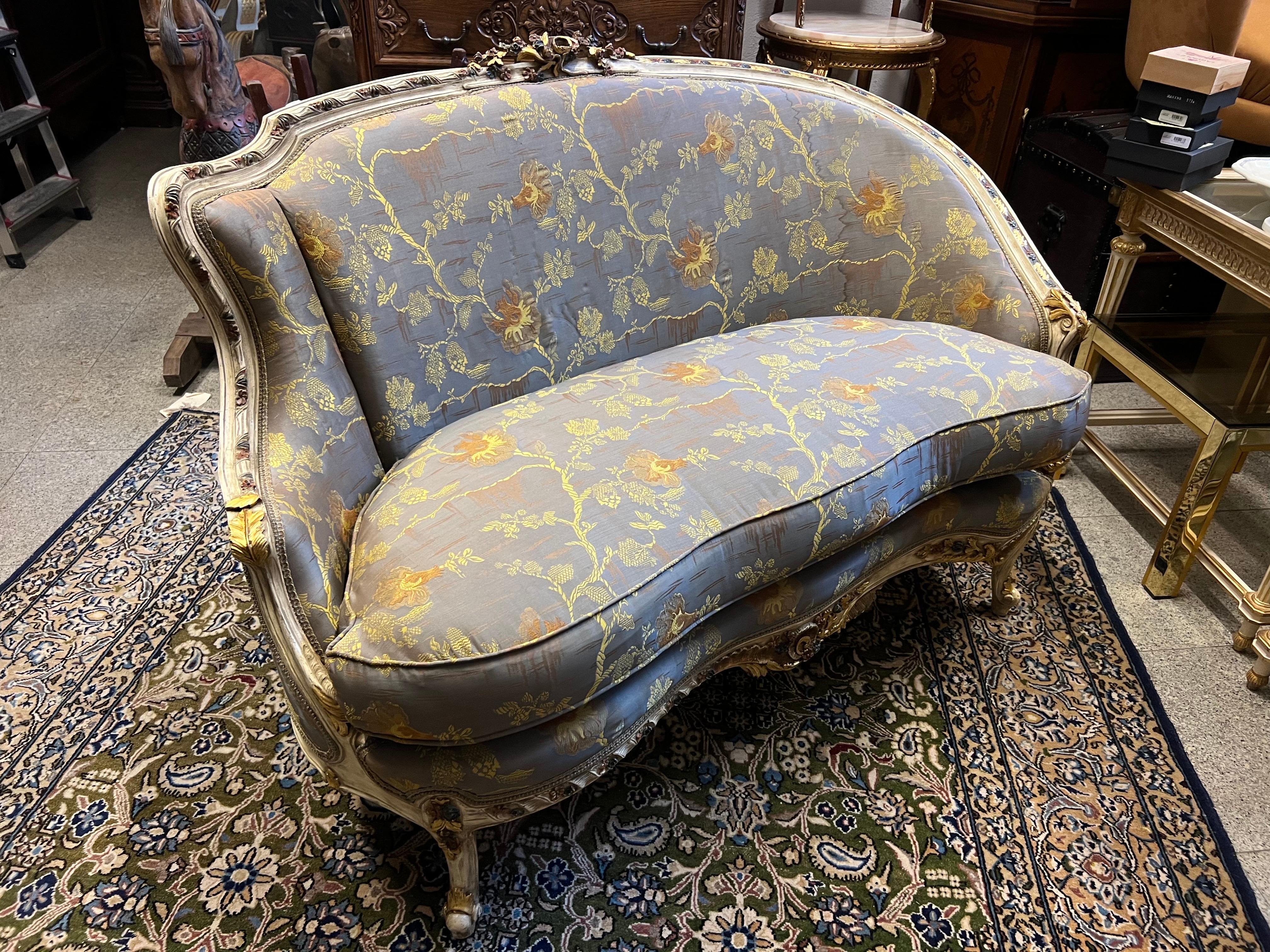 Petit canapé français à deux places avec un joli cadre sculpté et peint à la main avec de petits éléments floraux dans le style Louis XV. La pièce porte encore sa garniture d'origine en soie grise, qui présente de légers signes d'usure. La structure