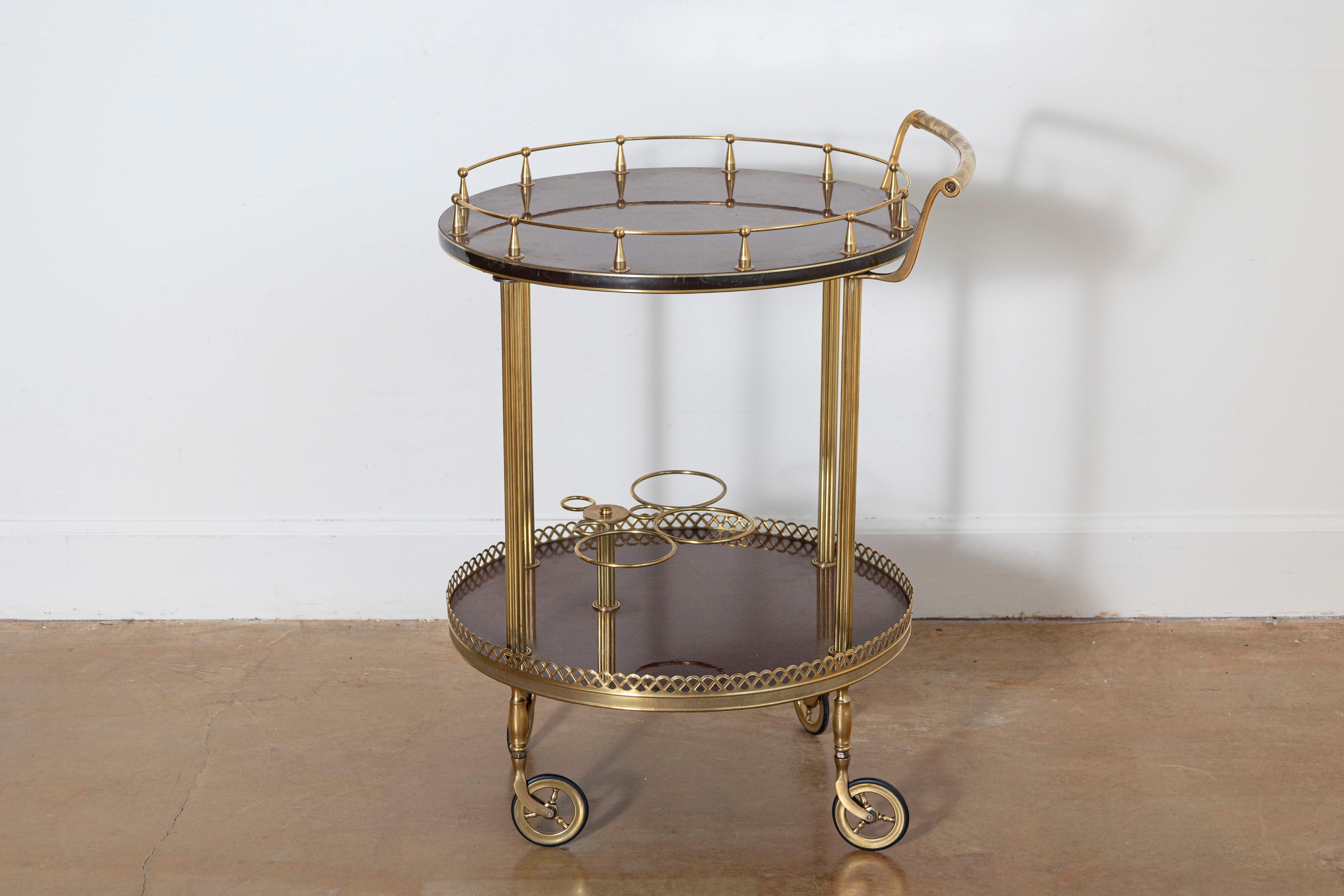 Ce chariot à boissons rond, fabriqué vers 1940, respire l'élégance et la sophistication dans le style de la Maison Jansen. Combinant le laiton et l'acajou, le chariot présente deux niveaux avec des surfaces en acajou encadrées par des galeries