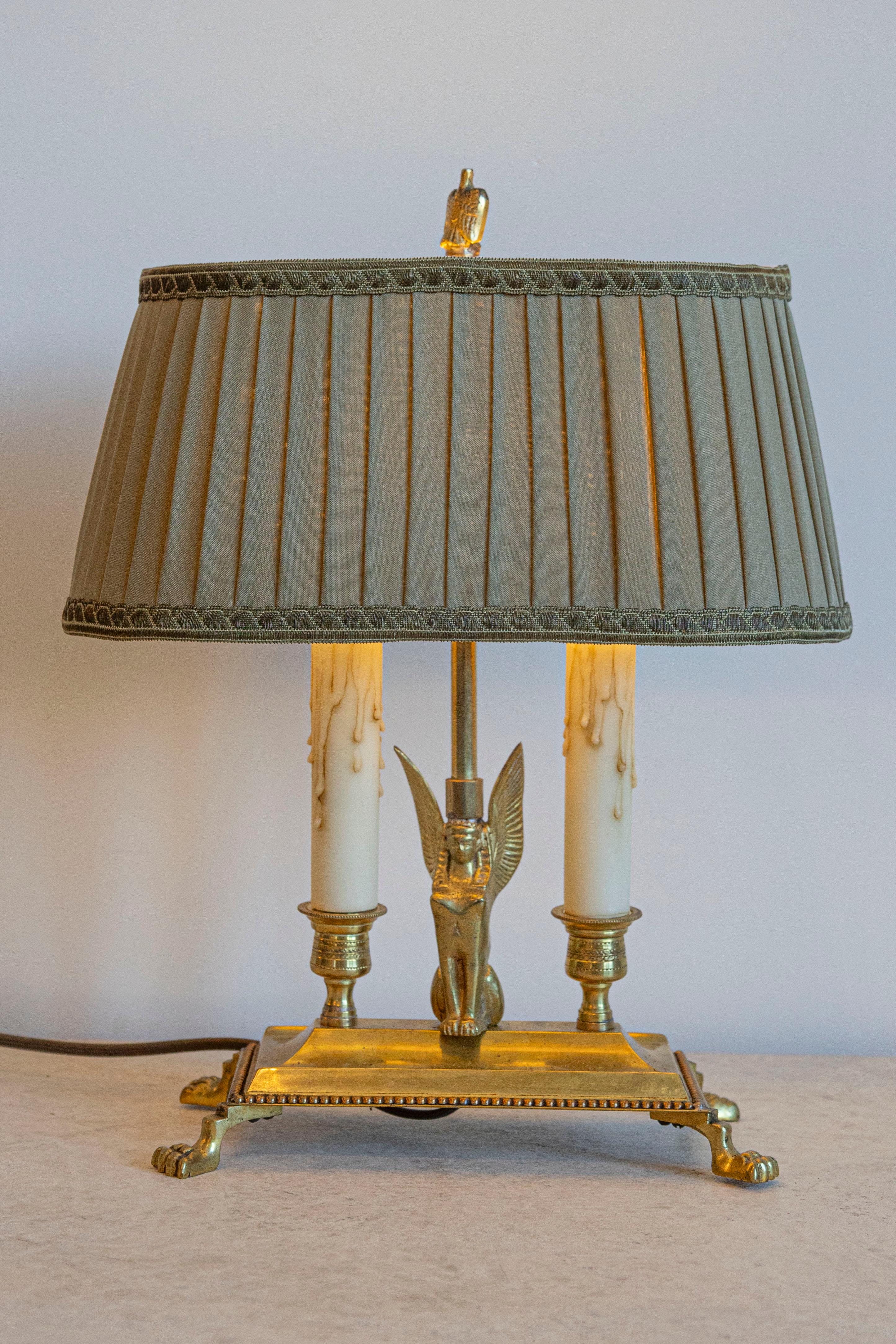 Cette exquise lampe bouillotte de style Empire français présente une élégante base en bronze doré ornée de détails finement moulés. La lampe repose sur quatre pieds griffus, avec une figure centrale de sphinx - une marque de fabrique du design