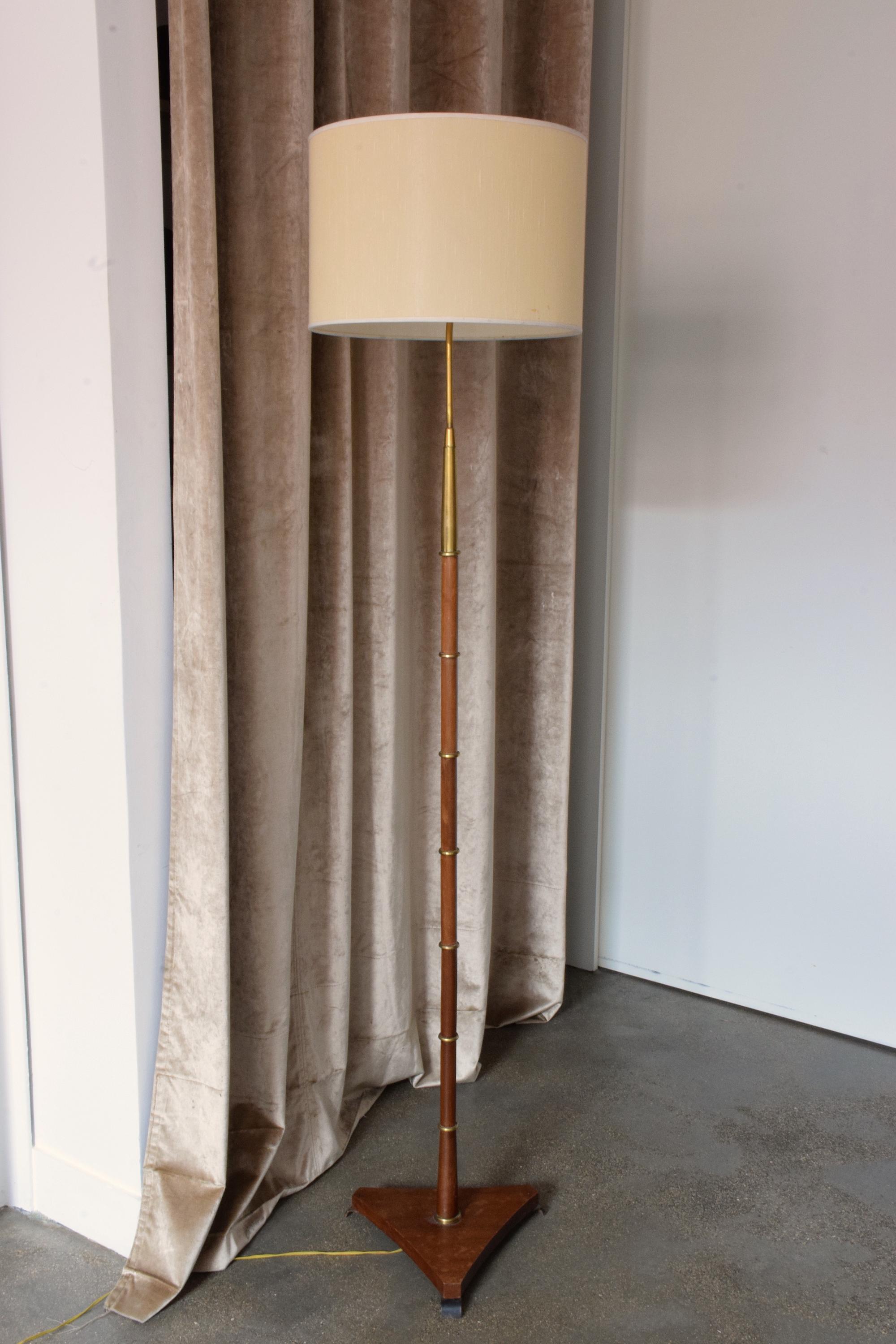 A 20th century French elegant floor lamp by Maison Lunel in its beautiful original condition designed in a solid wooden structure with delicate brass rings on the stem and a solid gold polished brass top. The triangular base sits on steel legs and