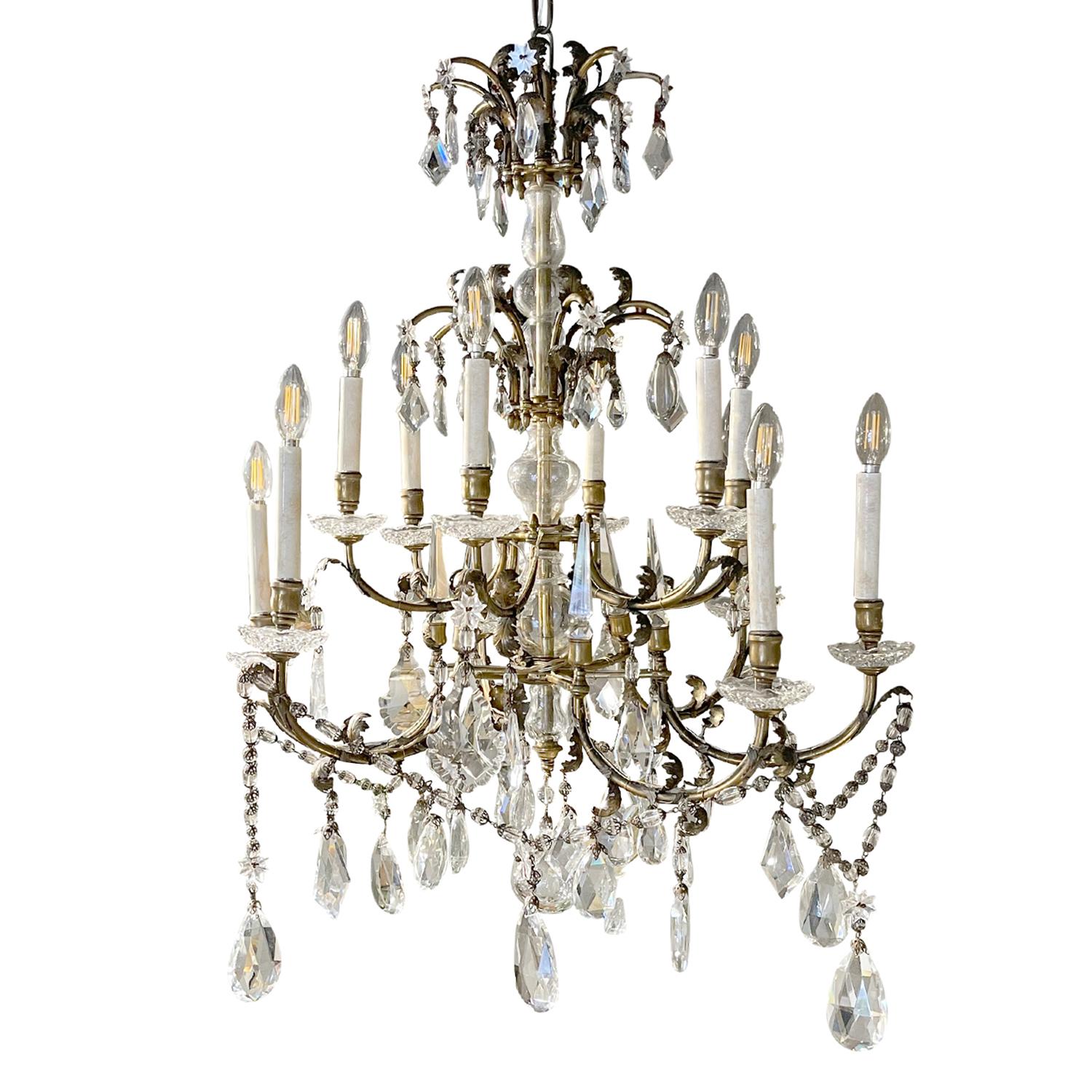 A vintage Art Deco French four tiered chandelier made of handcrafted metal and brass, in good condition. The frame of the teardrop ceiling light is made of bronze, composed with twelve scrolled arms, each of them is featuring a white waxed candle
