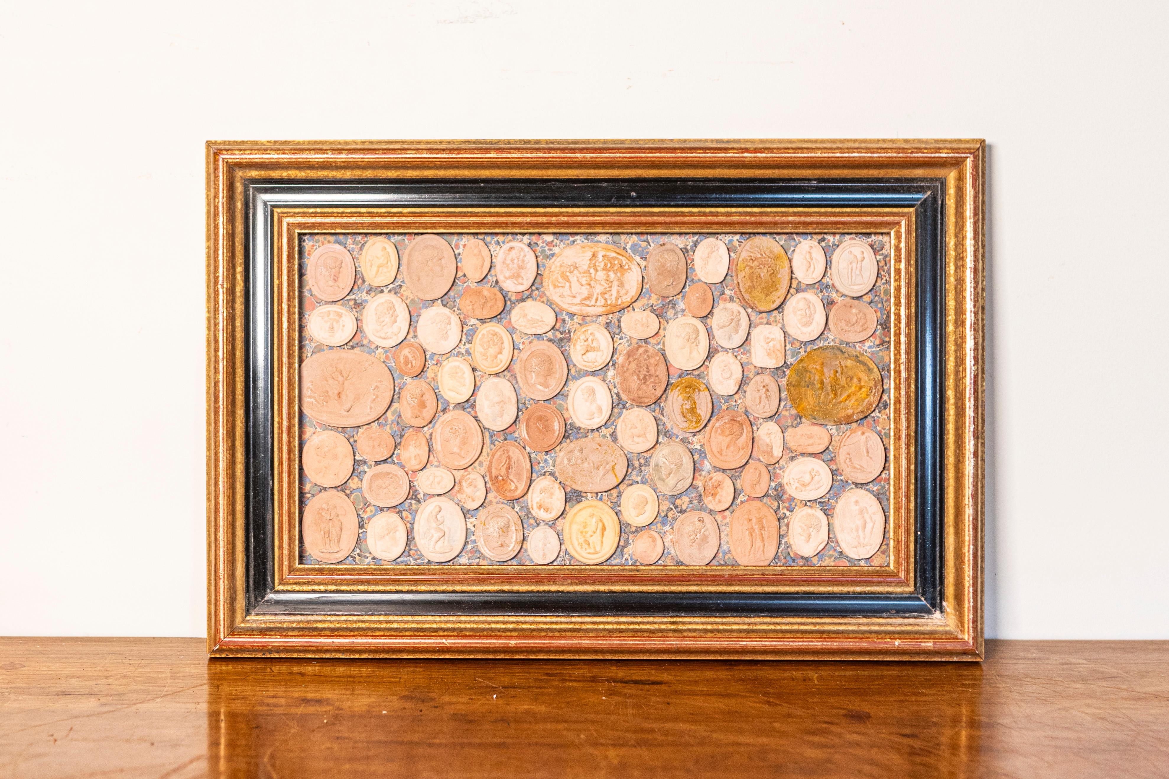 This unique 20th-century French collection features an exquisite arrangement of plaster intaglios and cameos, carefully mounted on a decorative marbled background and set within an elegant gilt and ebonized frame. The collection showcases a variety
