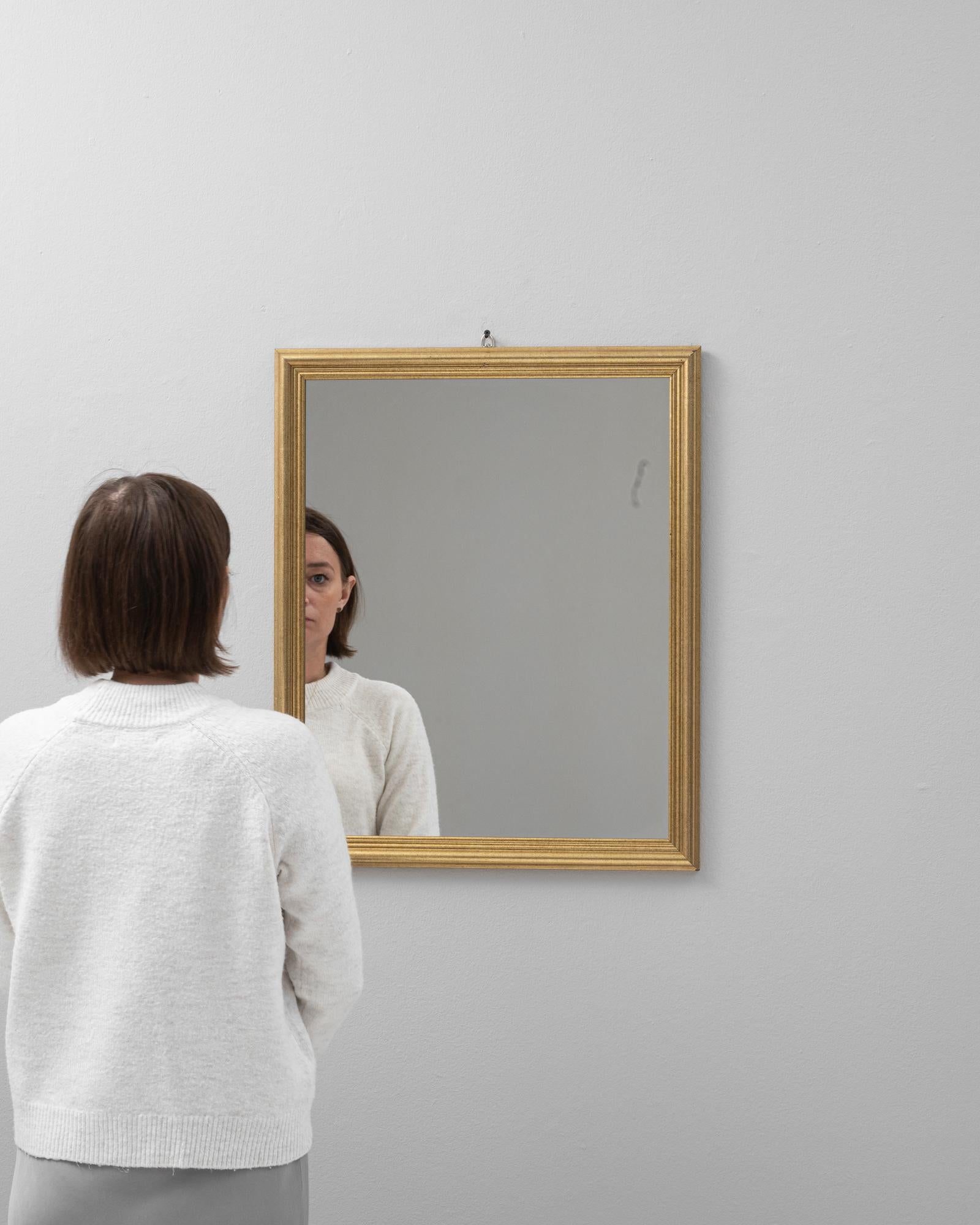 This 20th Century French gilded wood mirror presents a seamless blend of simplicity and splendor, ideal for bringing a touch of understated luxury to any space. The mirror's clean lines and classic square shape are accentuated by the subtle shimmer