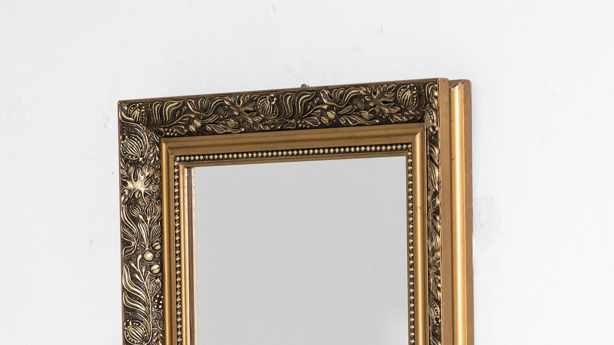 Indulge in the opulent charm of this 20th Century French Gilded Wooden Mirror. The intricate ornate details adorning the border showcase a wealth of golden foliage designs, elevating the mirror to a level of timeless elegance. The gilded surface