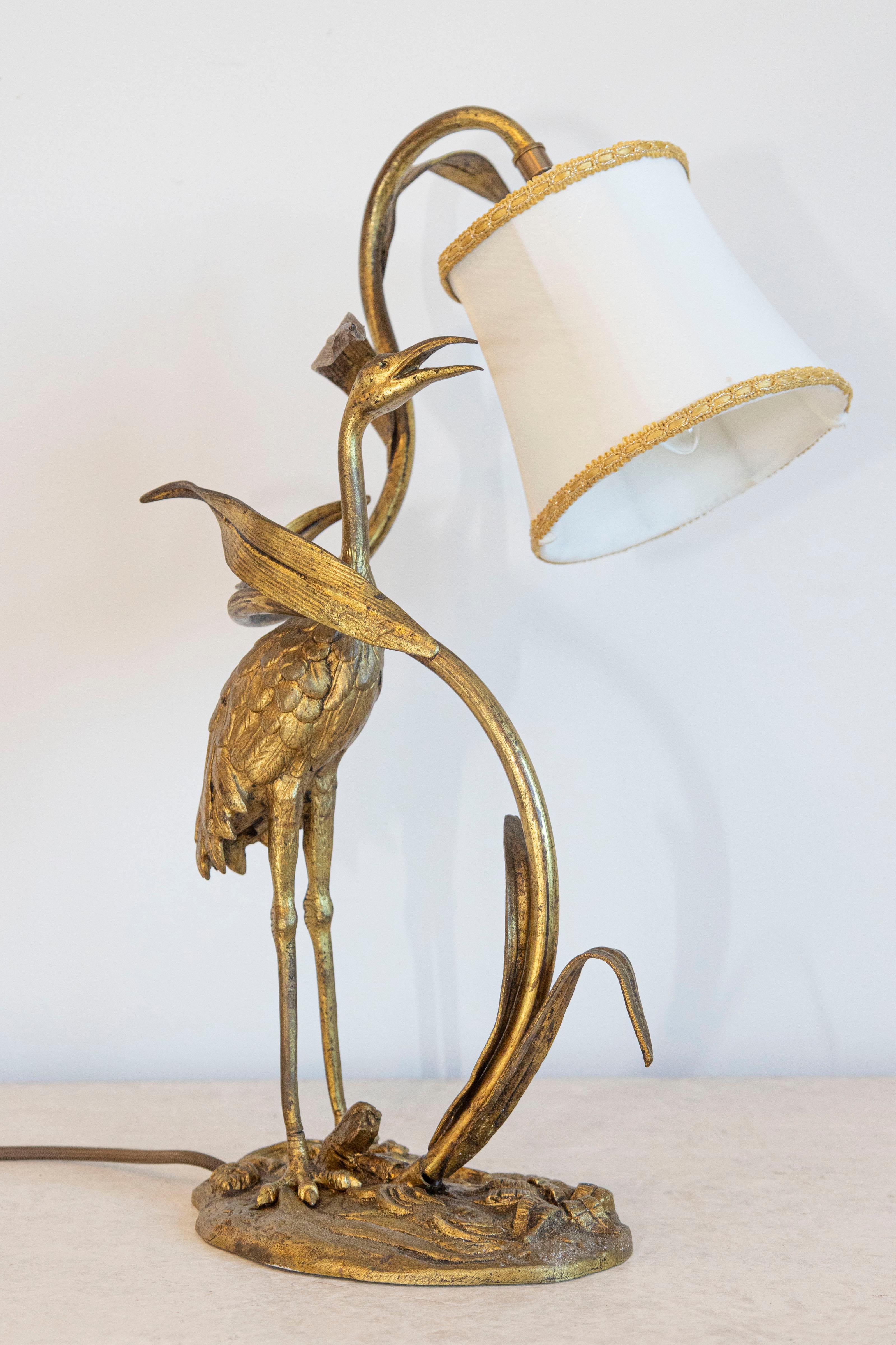 Cette ravissante lampe de table française du XXe siècle représente un héron aux détails exquis se tenant gracieusement parmi des roseaux, capturant ainsi l'essence du design Art nouveau. Le héron est réalisé en métal doré, ce qui confère à la pièce