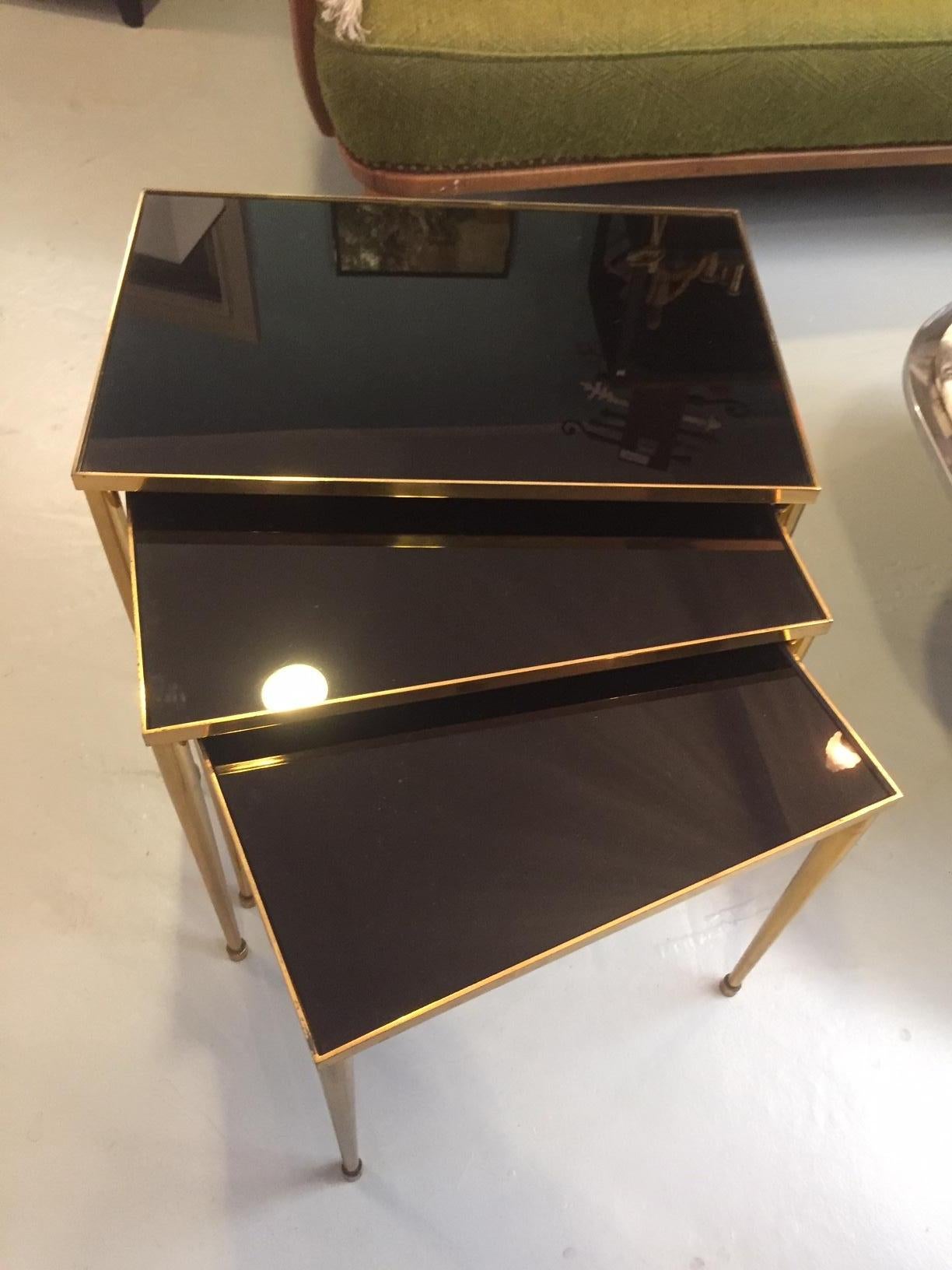 Beautiful set of three 20th century French gilded brass side table from the 1950s. 
The top is a smoked glass. Perfect condition.