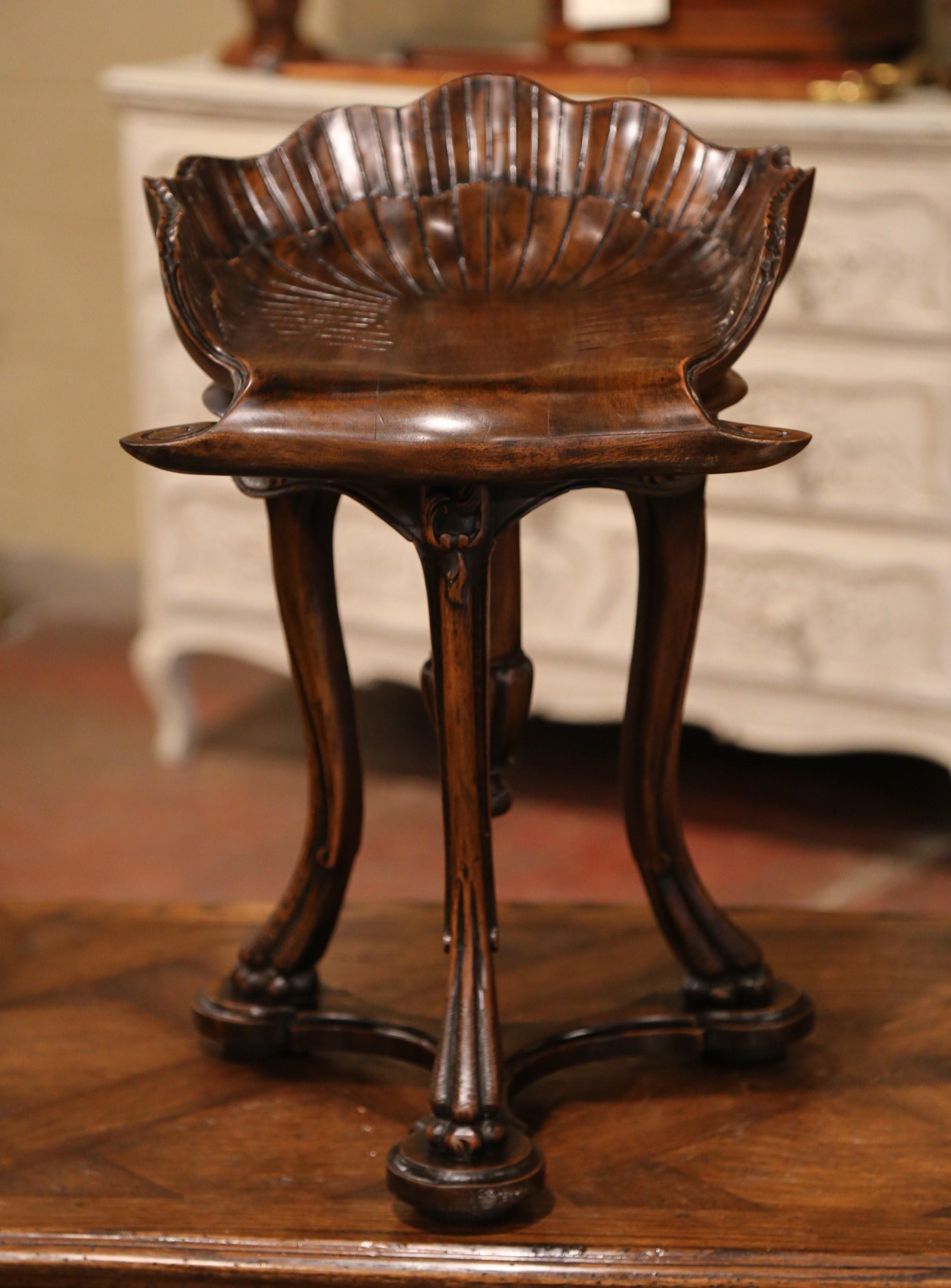 This carved antique fruitwood grotto stool was created in France, circa 1920. Perfect as a piano stool or simply a statement piece, the bench, stands on cabriole legs joined with bottom stretcher, and bun feet reminiscent of animal paws. The seat