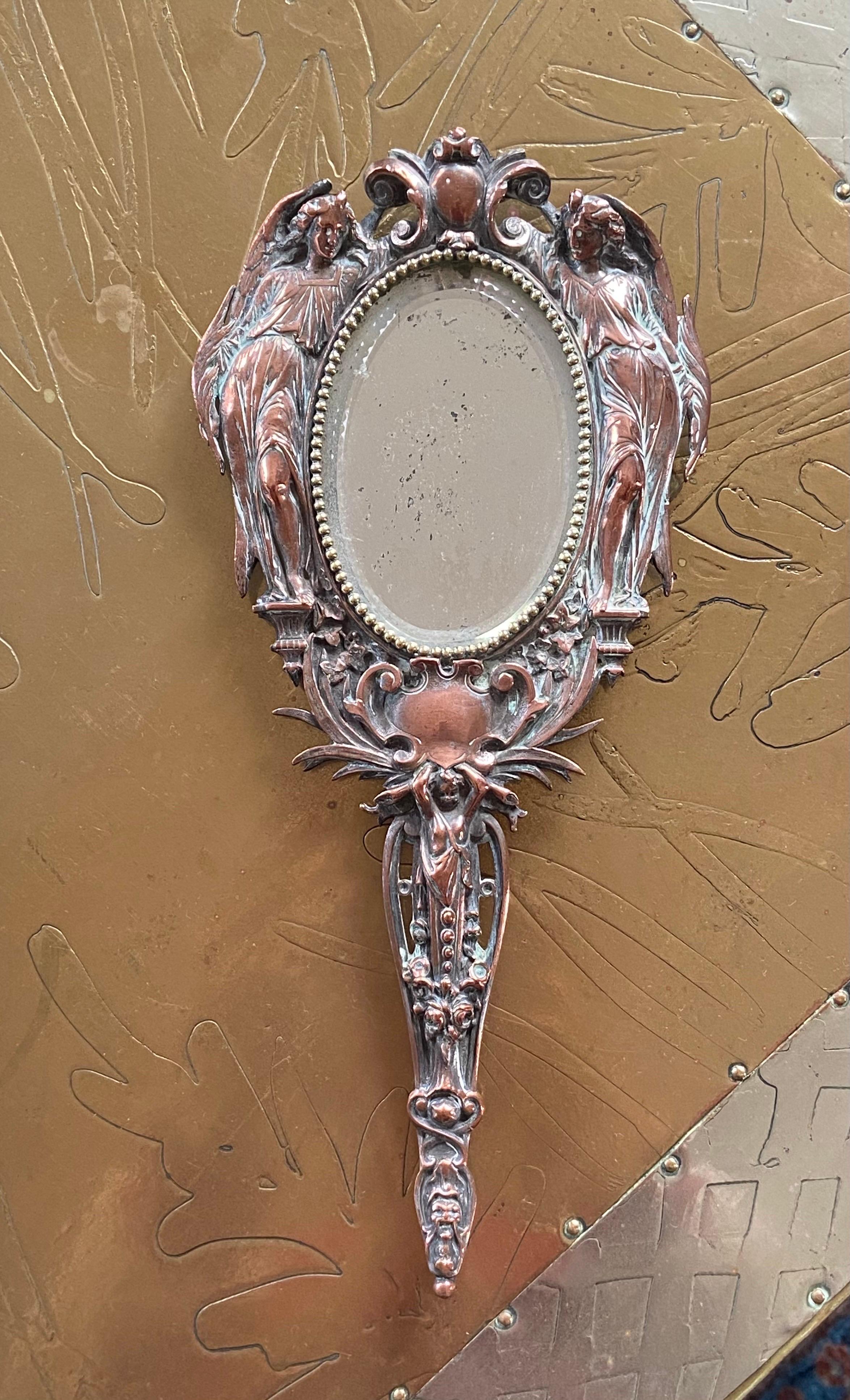 20th Century French hand mirror hand made in metal with two angels surrounding an oval mirror shape.
France, circa 1930.