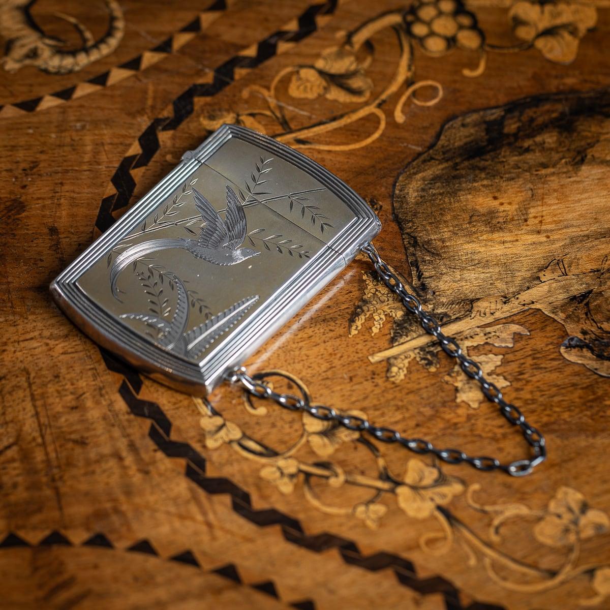 Portasigarette d'argento massiccio europeo del XX secolo. Il fronte presenta un uccello in volo tra le foglie, mentre il retro mostra un semplice motivo di foglie. Il design evidenzia incisioni in argento su uno sfondo dorato. Una piccola catena è