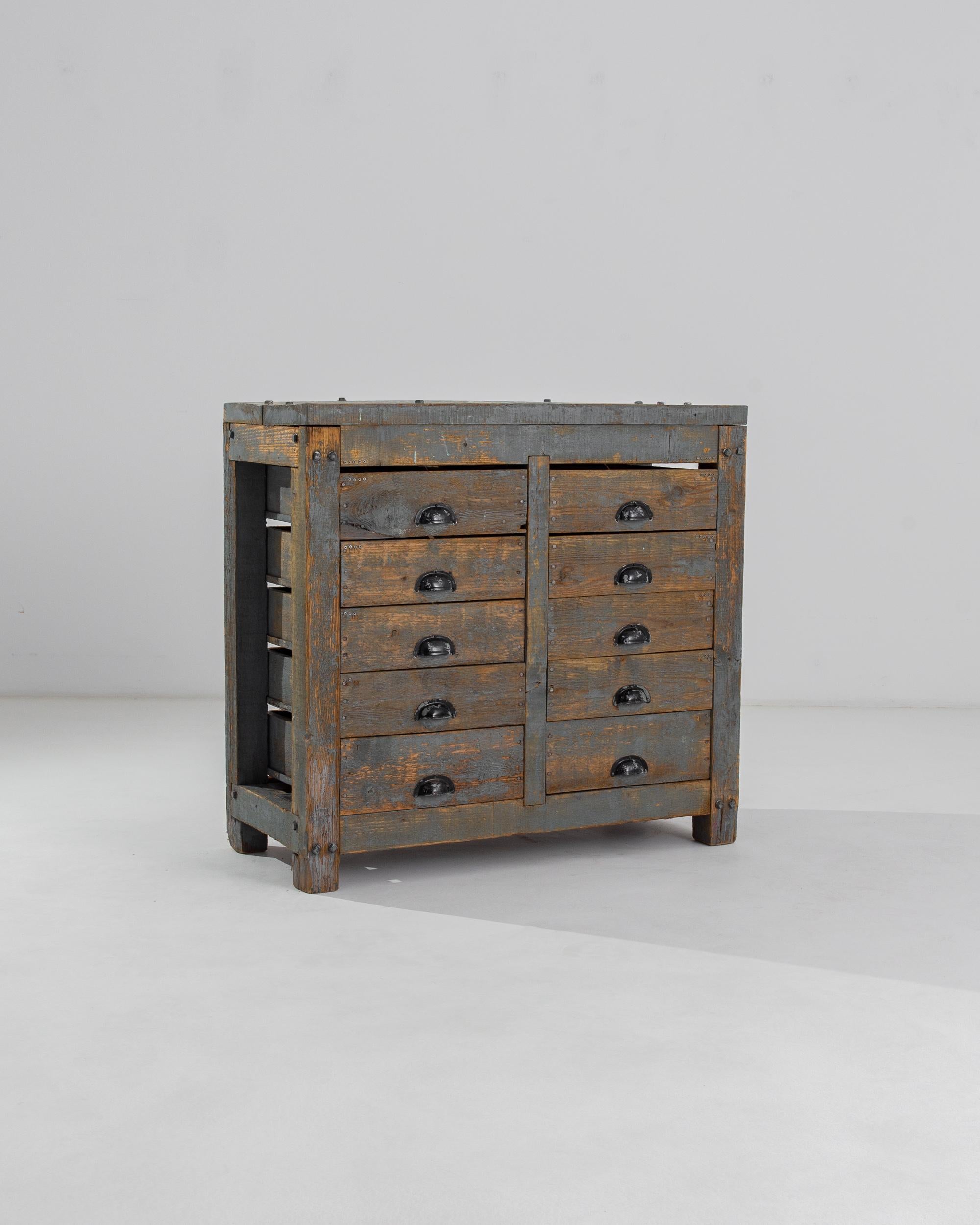This industrial work table holds a chest of drawers with a unique, timeworn patina. Made in France in the 20th century, a series of ten drawers are arranged in two columns within a sturdy wooden frame. The cabinet has no back or sides, and the