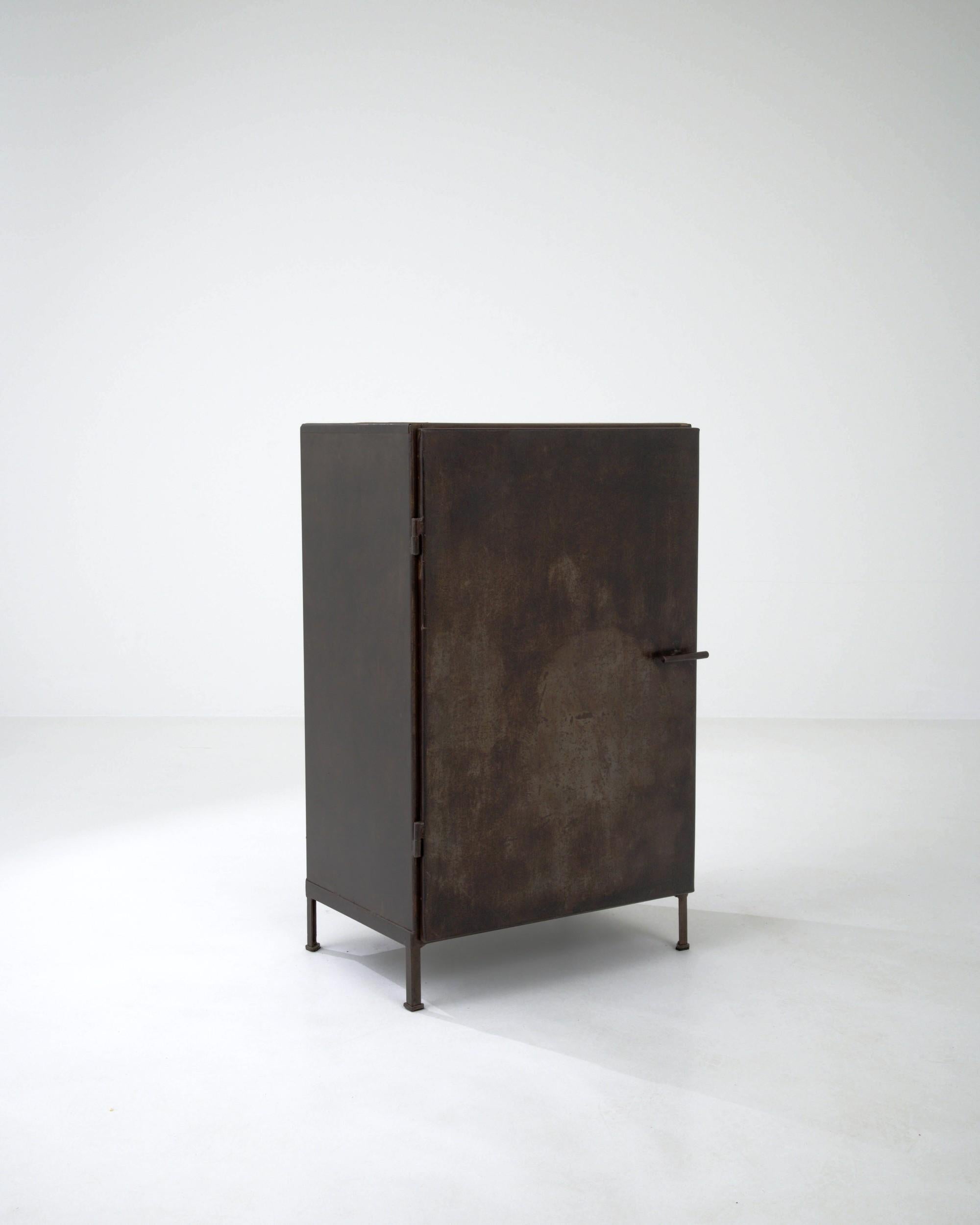 The minimalist shape and rich patina of this vintage metal cabinet make for a striking Industrial find. Made in France in the early 20th century, the design possesses a rational simplicity: clean corners and a bold refusal of ornamentation create a