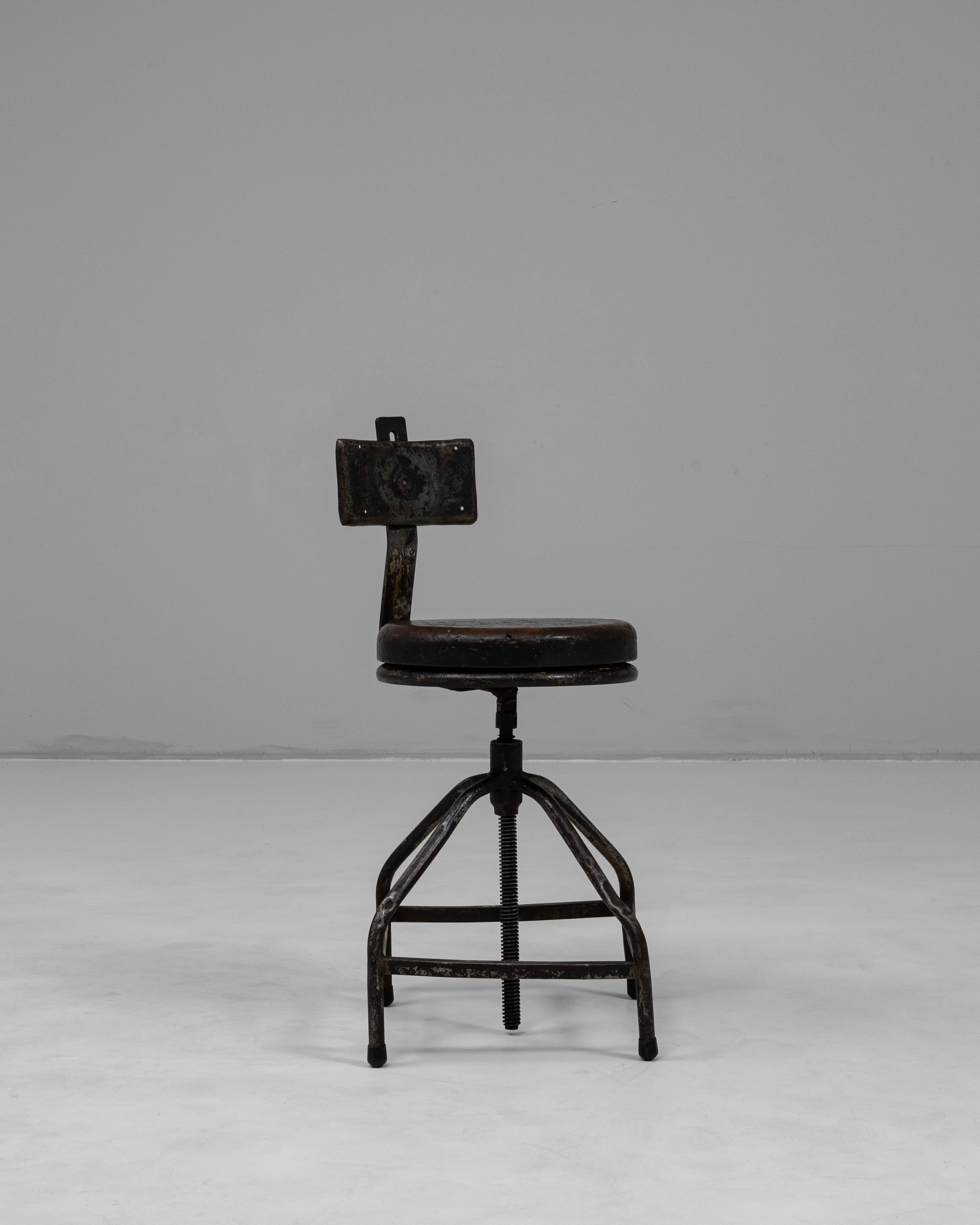 Cette chaise pivotante industrielle française du 20e siècle incarne un design utilitaire au caractère durable. Construite en métal solide, la chaise présente une base sculpturale avec des supports incurvés et une colonne centrale filetée qui permet
