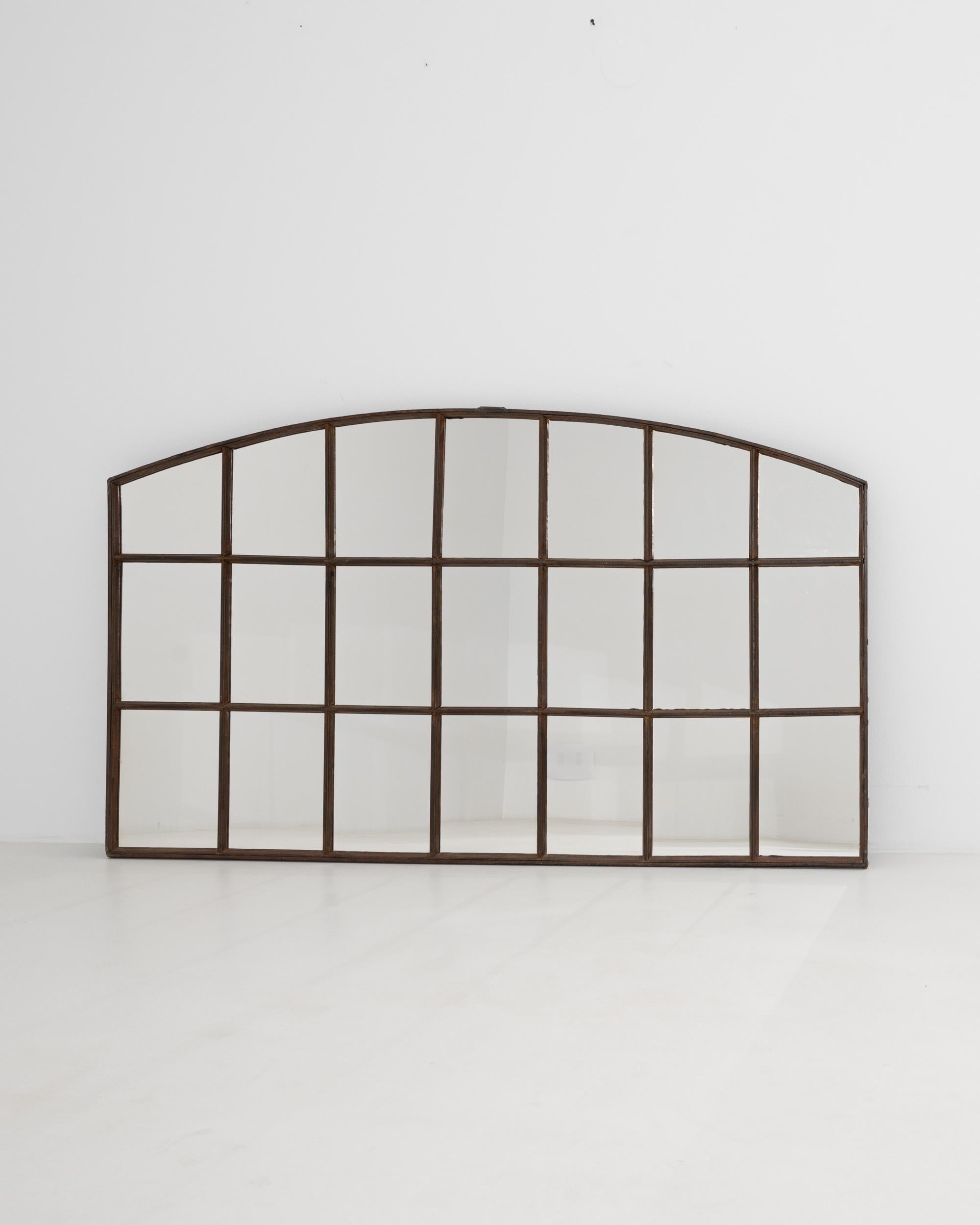 Architectural and striking, this Industrial iron mirror would once have opened the walls of a factory. Made in France in the 20th century, the form evokes a large window; mirrored panes serve to maximize the natural light within a space. The curve