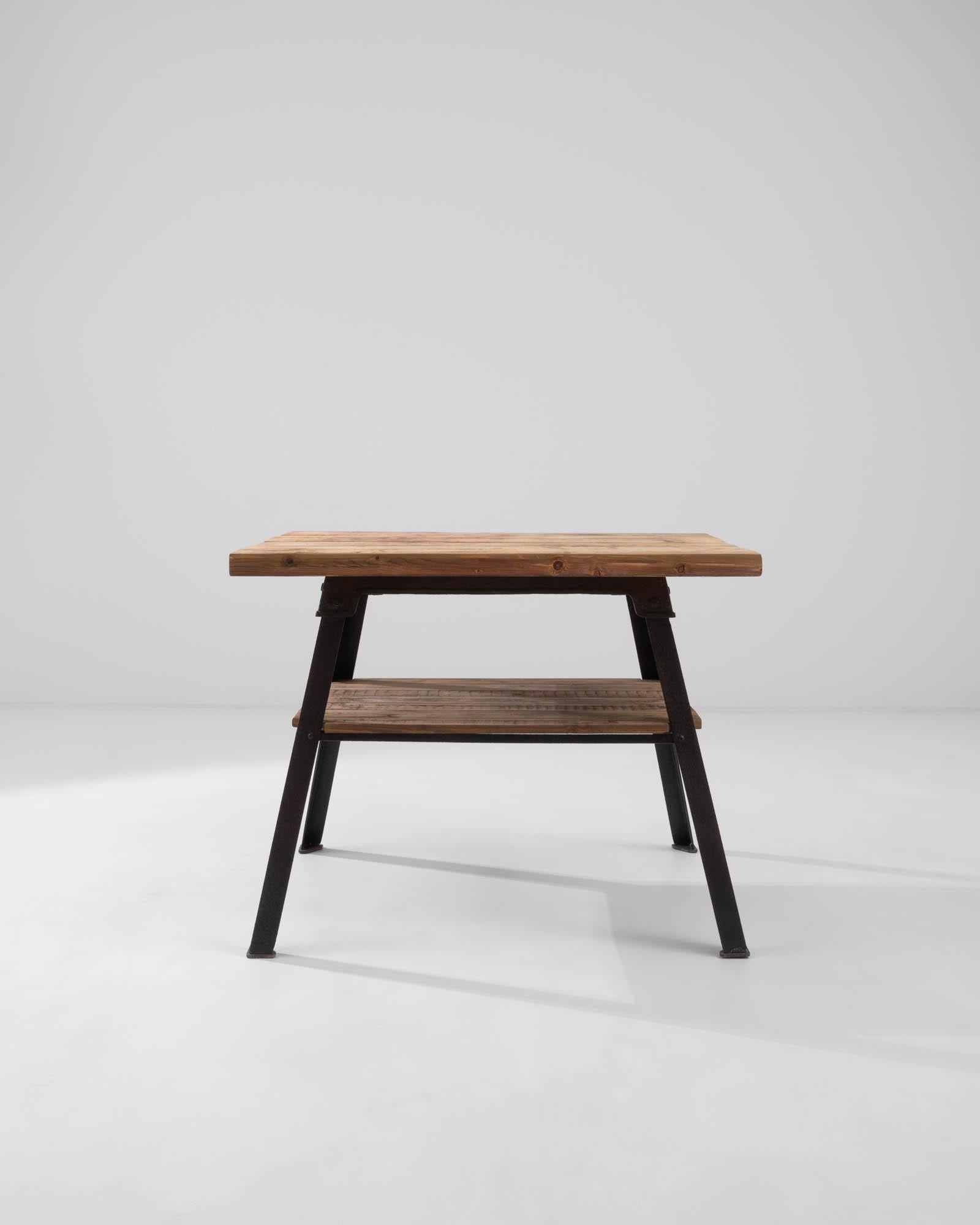 Stylish yet sturdy, this Industrial table offers a compelling vintage find. Built in France in the 20th century, a tabletop of natural wooden boards sits atop a cast iron frame. The bold angles of the legs create a striking trapezoid profile,