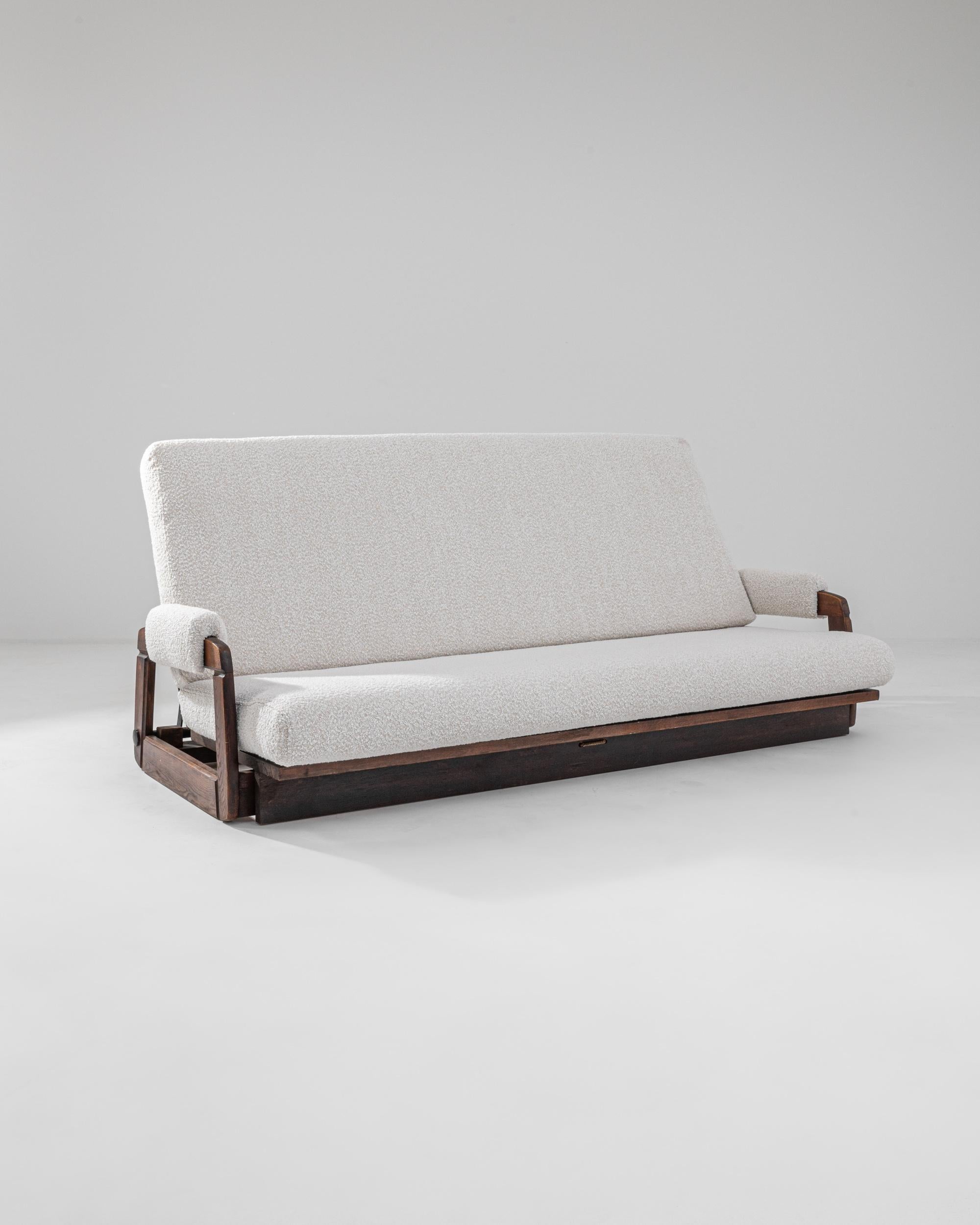 A wooden upholstered sofa made in mid-20th century France. A soft ivory boucle upholstery brings a fresh modern look to this vintage gem. The back of this adaptable piece folds down to transform the sofa into a bed, a space saving feature for
