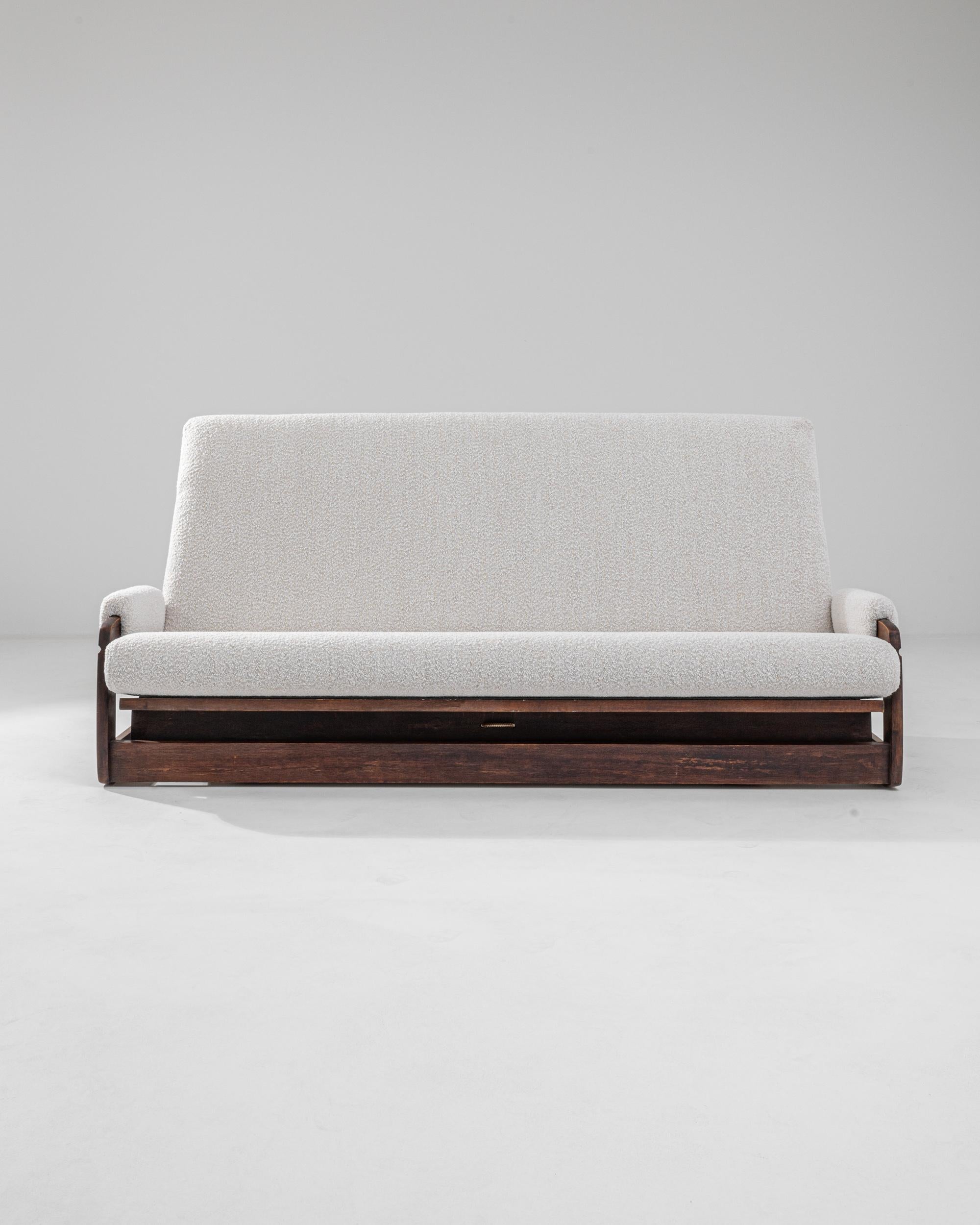 A wooden upholstered sofa made in mid-20th century France. A soft ivory boucle upholstery brings a fresh modern look to this vintage gem. The back of this adaptable piece folds down to transform the sofa into a bed, a space saving feature for