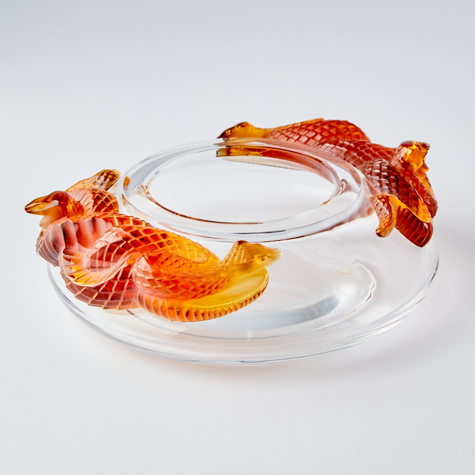 Este exquisito cuenco decorativo de mediados del siglo XX de Lalique muestra el reconocido arte y la artesanía de la marca. El cuenco tiene una forma circular achaparrada de vidrio incoloro, acentuada por unas llamativas asas en forma de serpiente