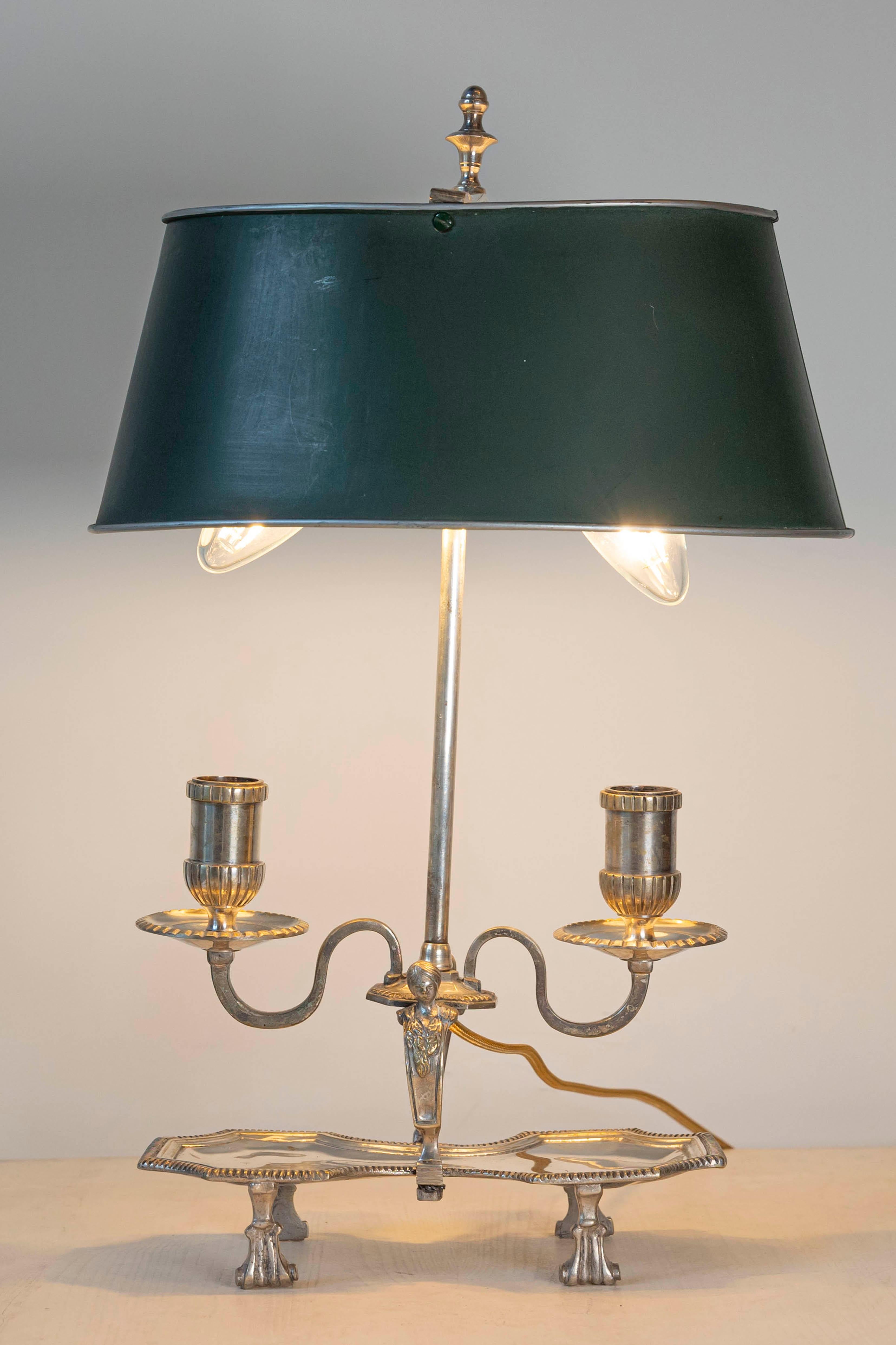 Cette lampe bouillotte française du XXe siècle dégage une élégance intemporelle, alliant fonctionnalité et raffinement artistique. Fabriquée en métal argenté, la lampe présente deux bras gracieusement incurvés avec des douilles détaillées de type