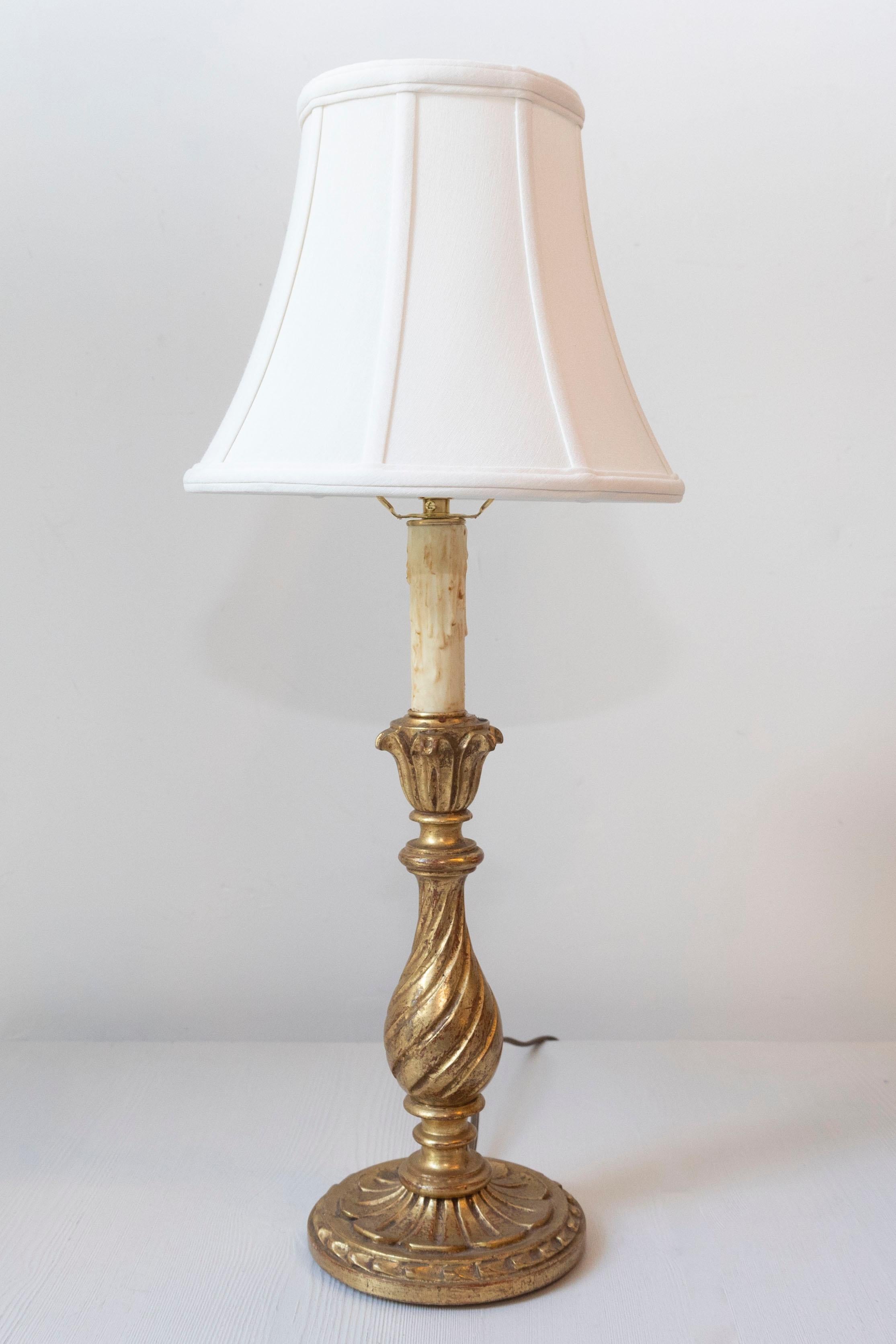 Questa lampada in legno dorato del XX secolo emana un'eleganza senza tempo grazie al suo design classico e alla doratura originale in foglia d'oro, che si mantiene in ottime condizioni. La base scolpita presenta una colonna graziosamente