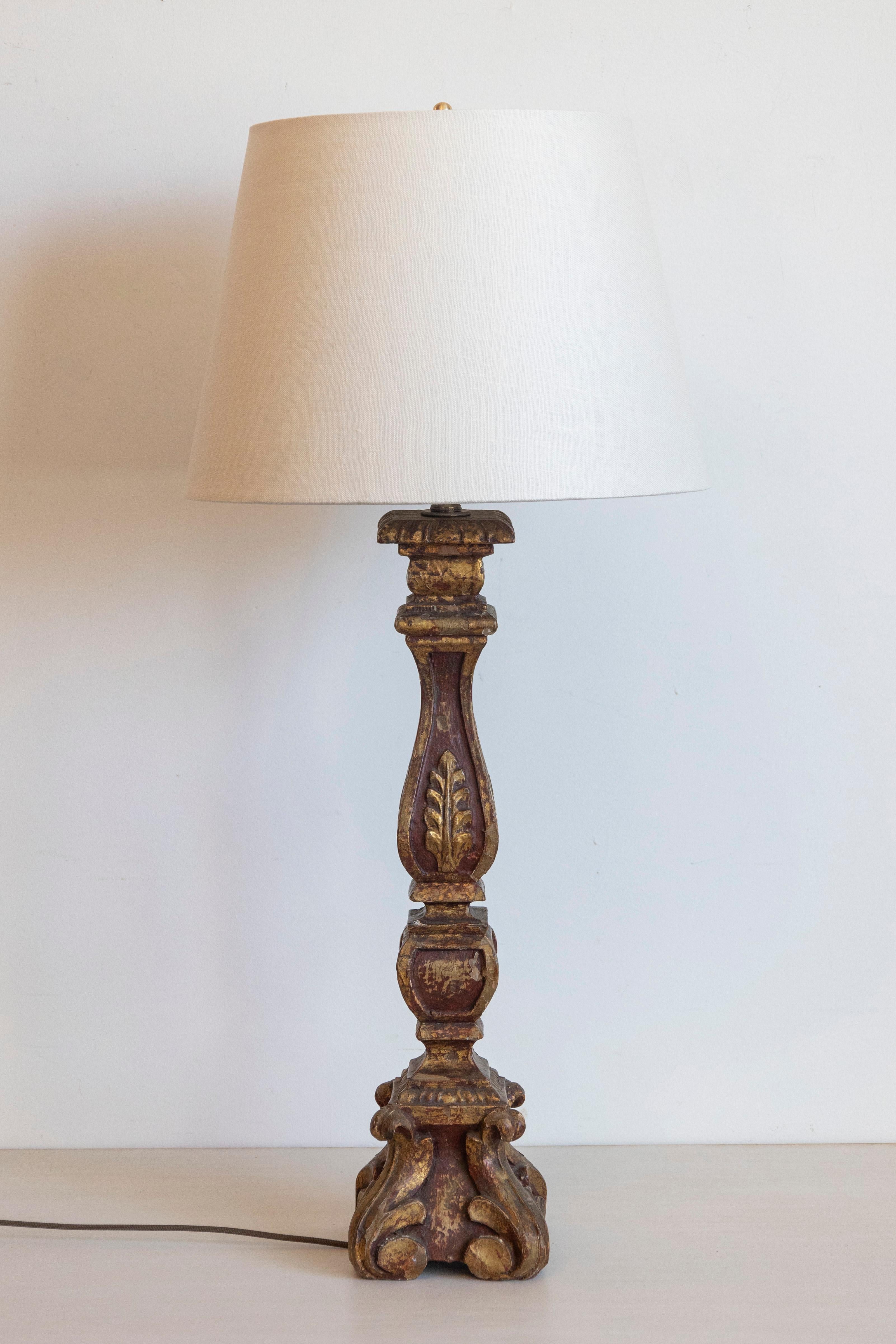 Esta lámpara de mesa, elegante y con clase, tiene una base de madera antigua bellamente elaborada con un rico fondo rojo oscuro y tallas doradas, que desprende encanto y sofisticación del viejo mundo. La columna, finamente tallada, presenta motivos