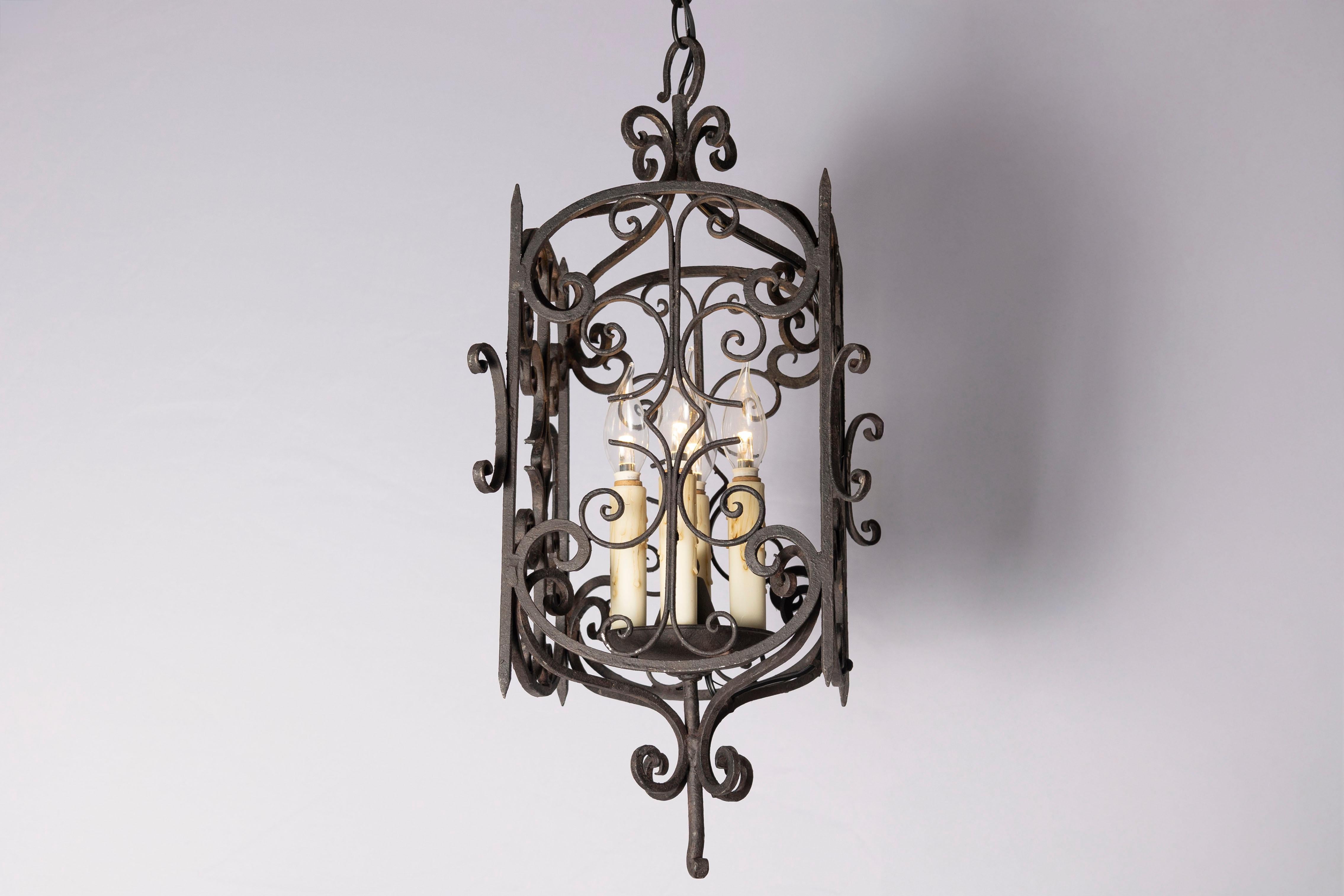 Questa elegante lanterna francese del XX secolo mostra l'arte senza tempo della lavorazione del ferro battuto. L'intricata lavorazione a volute è caratterizzata da delicate curve e fiocchi, creando un design simmetrico e traforato che emana