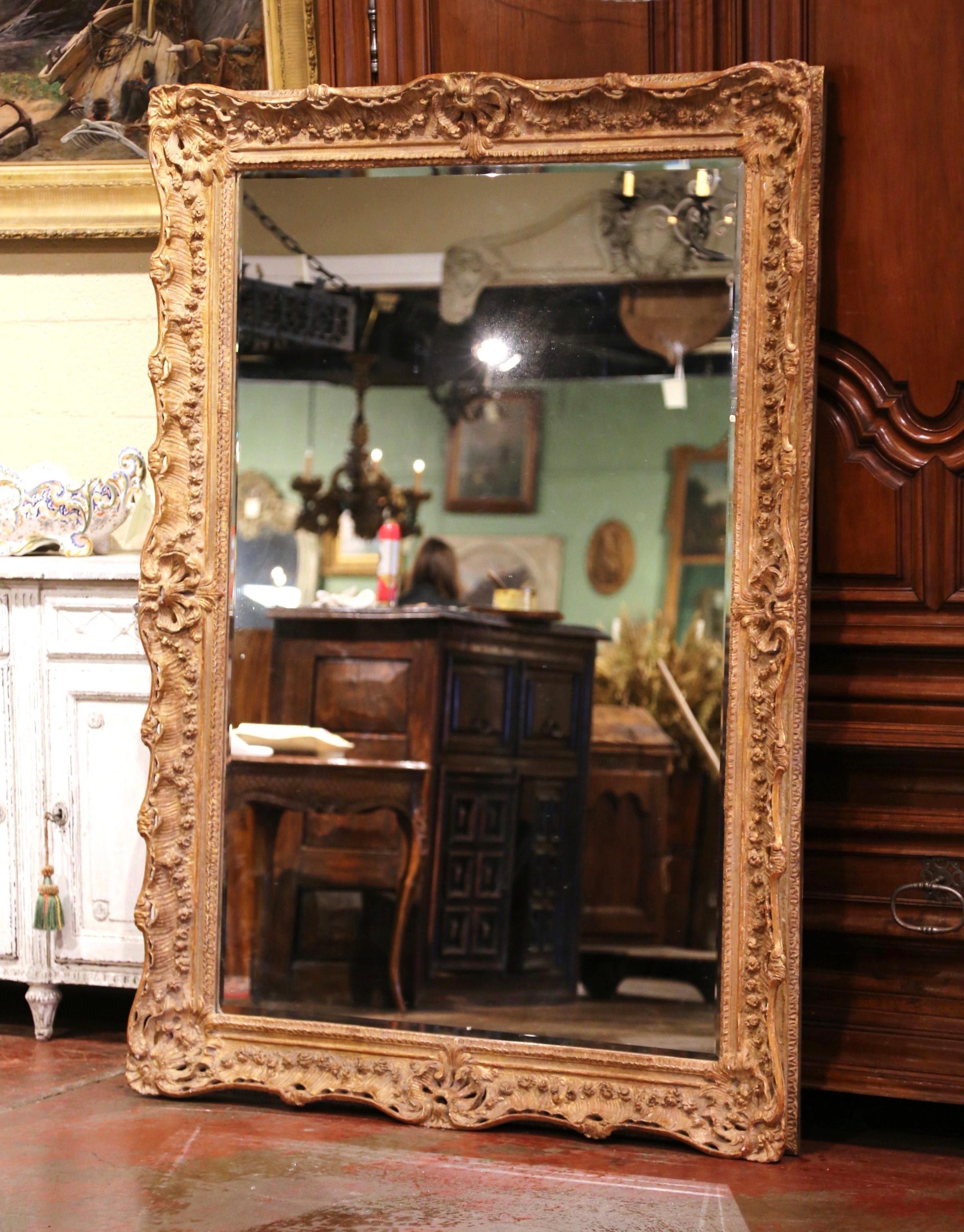 This elegant mirror was created in France, circa 1950. Rectangular in shape, the large mirror can be hang vertically or horizontally; the frame features exquisite hand carved floral decor, and is embellished with a cartouche shell motif in each