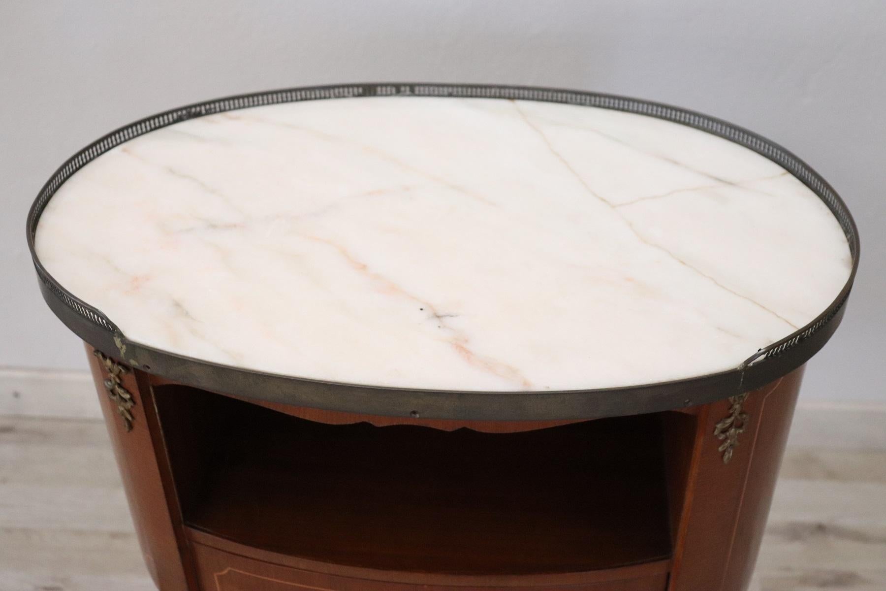 Elegant oval bedside table in Louis XV style richly adorned with gilded and chiselled bronzes with a practical drawer on the front and a storage compartment. The top is in white marble with light and delicate veins on the gray and pink present a