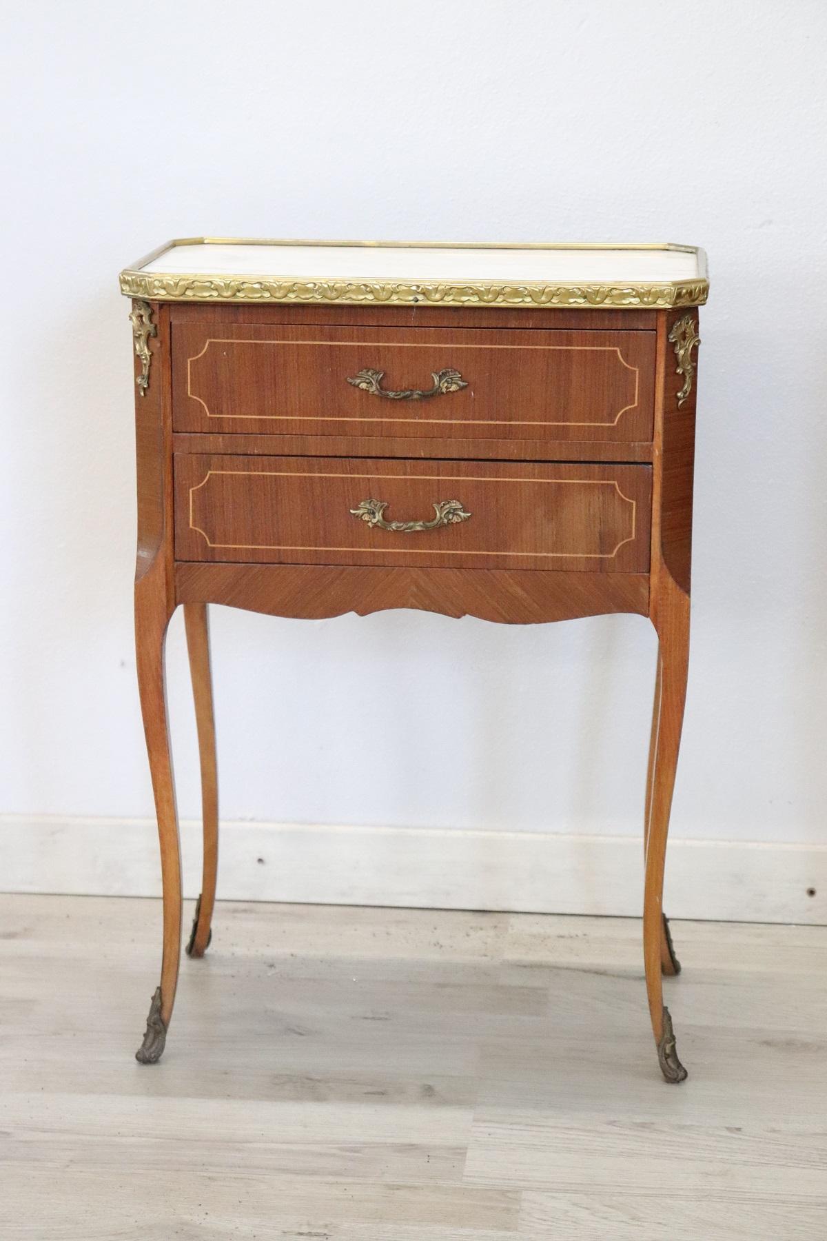 Louis XV style furniture richly adorned with gilded and chiselled bronze. The wood has a delicate geometric inlay. The top is in precious white marble with light grey and pink veins. A pair of really elegant bedside tables, ideal in the bedroom but