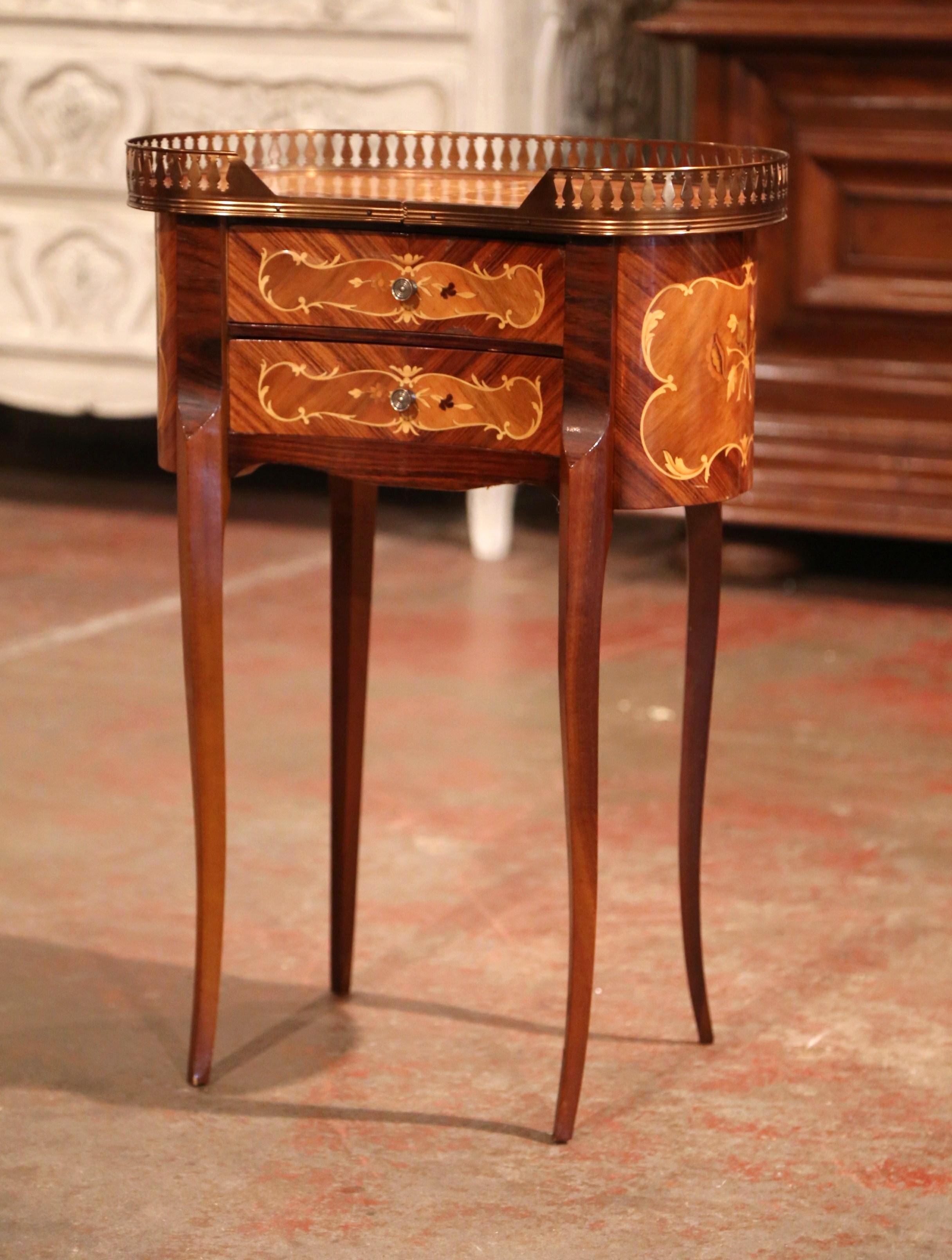 This elegant kidney shape fruitwood commode was crafted in Paris, circa 1980.The petite chest sits on slim cabriole legs and features two drawers with floral inlay decor and embellished with brass pulls. The top with an inset brass pierced gallery