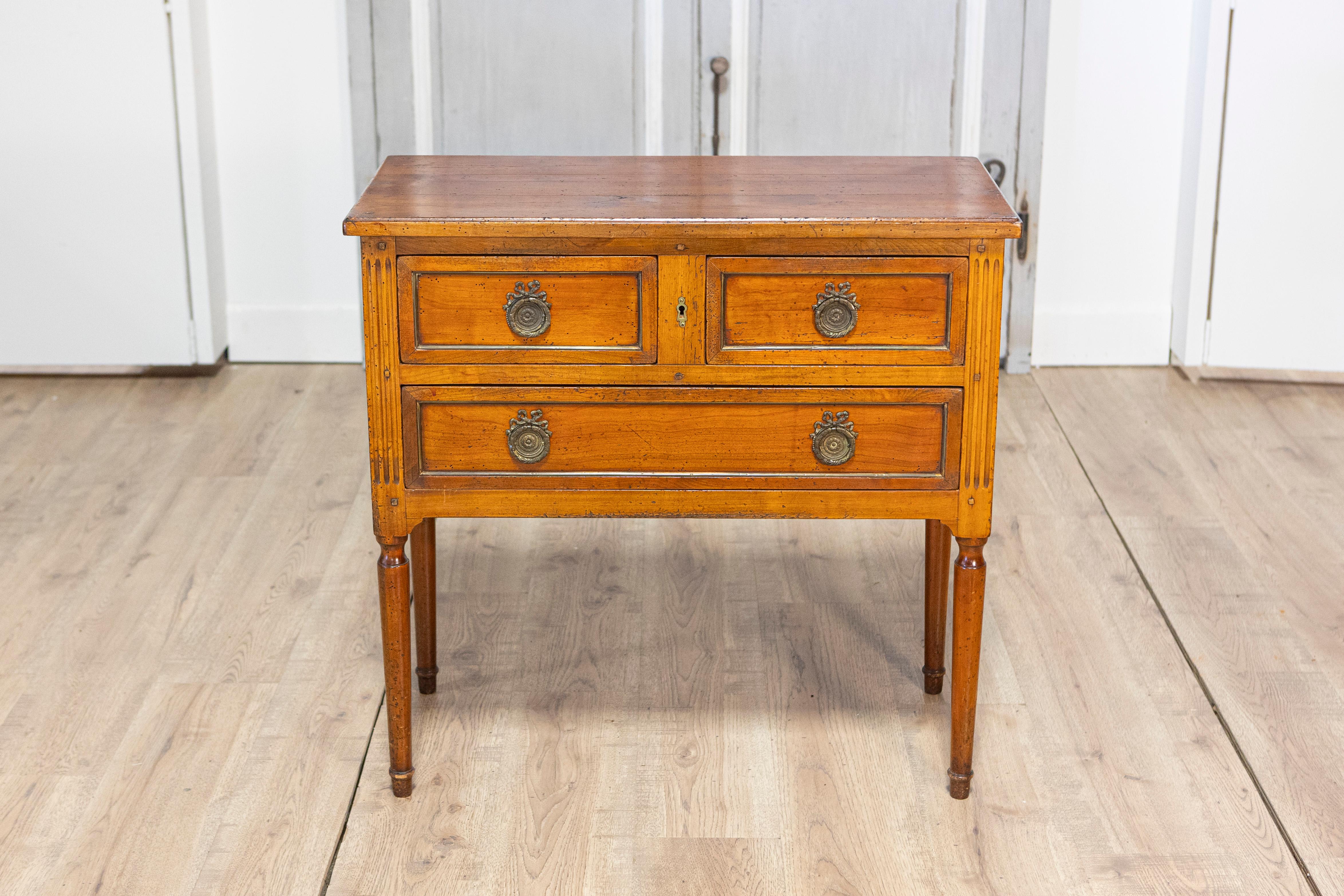 Questa piccola commode elegante e di classe, realizzata in stile Luigi XVI durante il XX secolo, combina un design senza tempo con una pratica funzionalità. Realizzato in legno di frutta dai toni caldi, presenta tre cassetti disposti su due file,