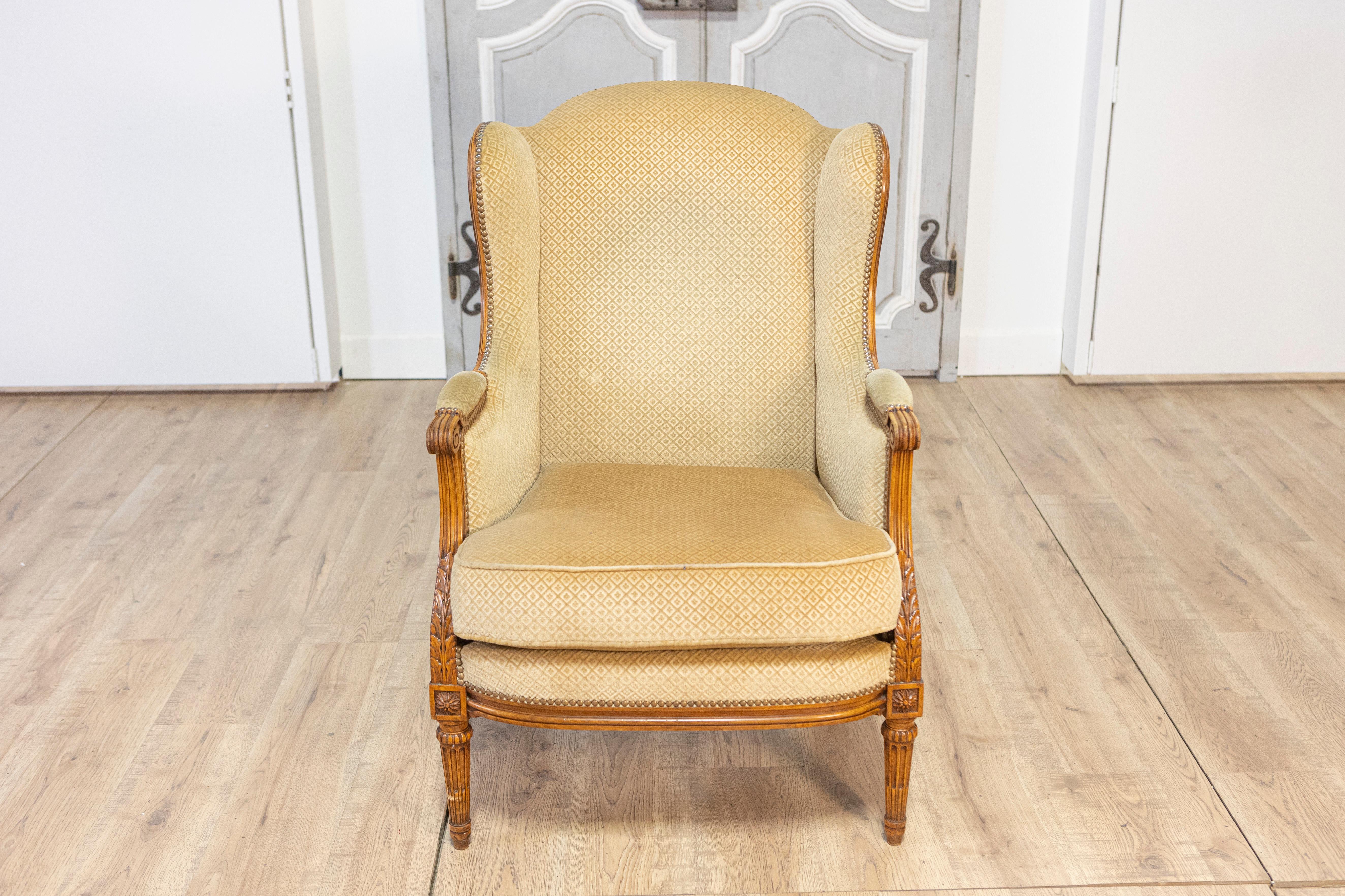 Esta elegante bergère o silla de pastora francesa del siglo XX, de estilo Luis XVI, combina una sofisticación atemporal con una artesanía excepcional. El armazón de madera maciza de haya presenta intrincadas tallas, como patas estriadas y detalles